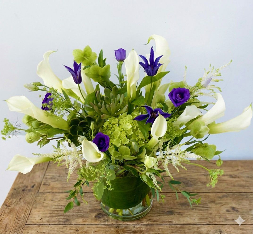White calla lilies and purple flowers in a glass vase