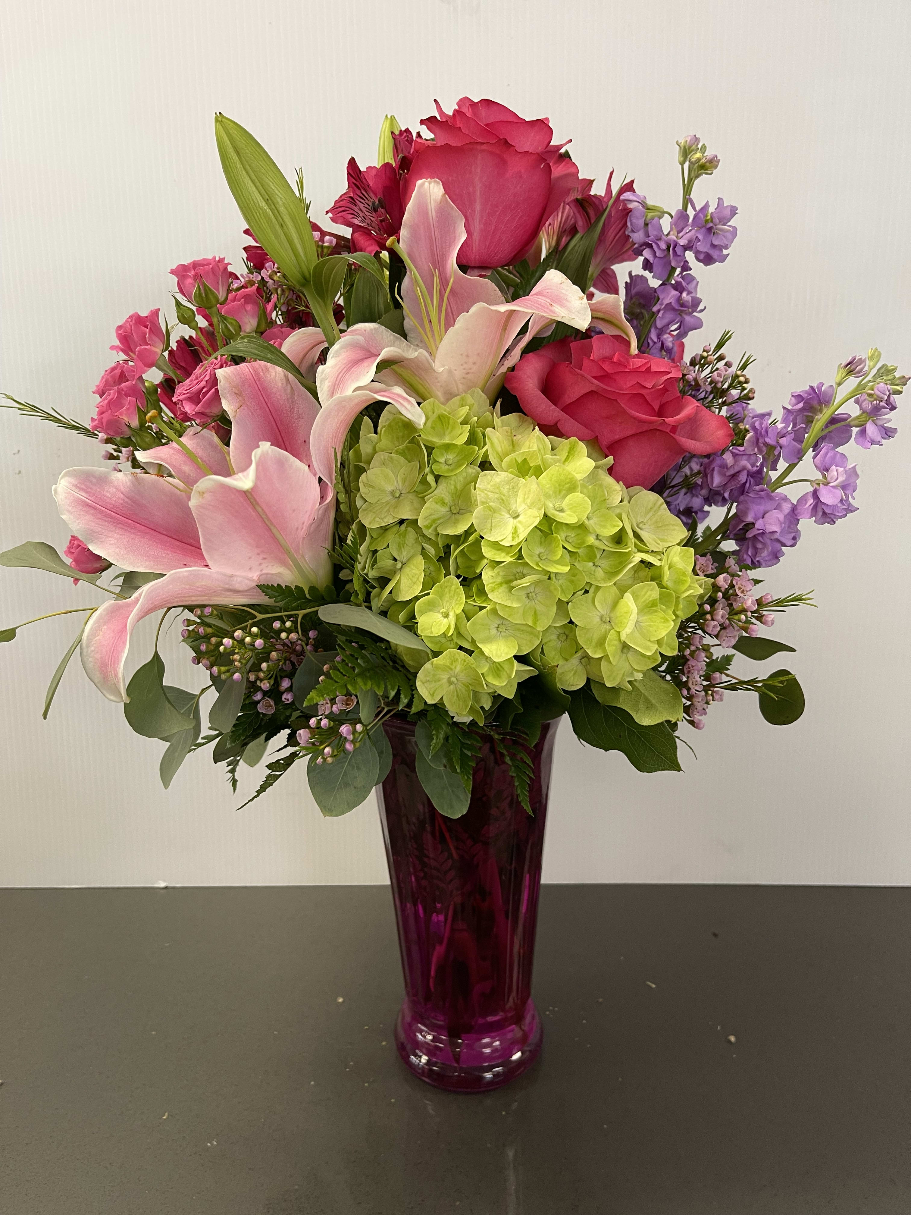 Pink lilies, roses, hydrangea, and purple flowers in a magenta vase