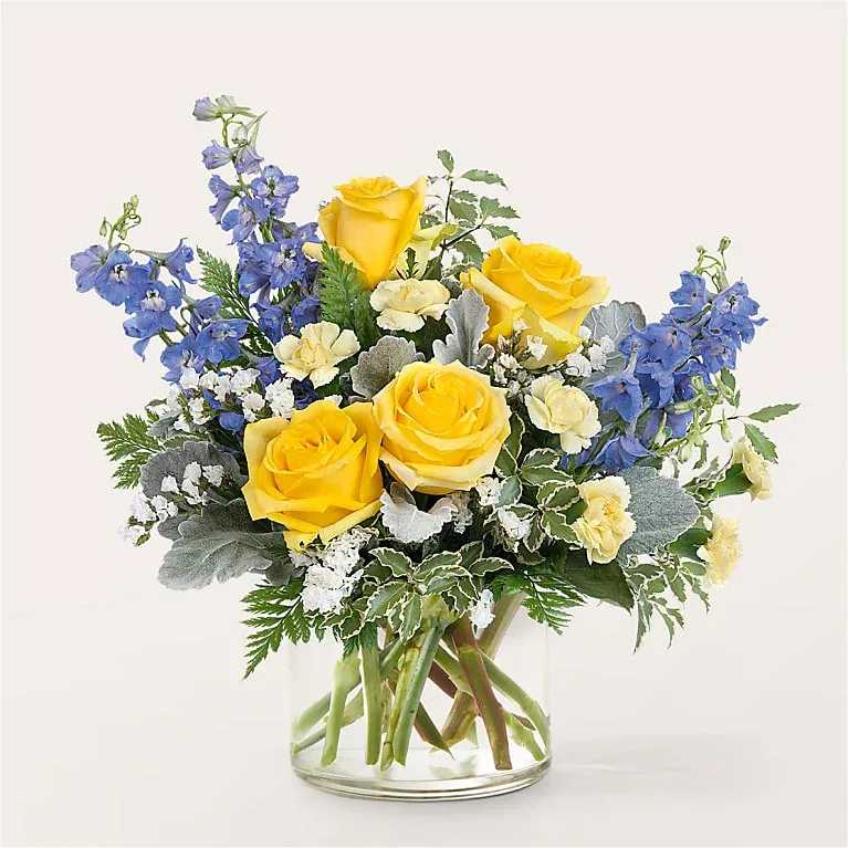 Yellow roses and blue delphinium in a clear glass vase