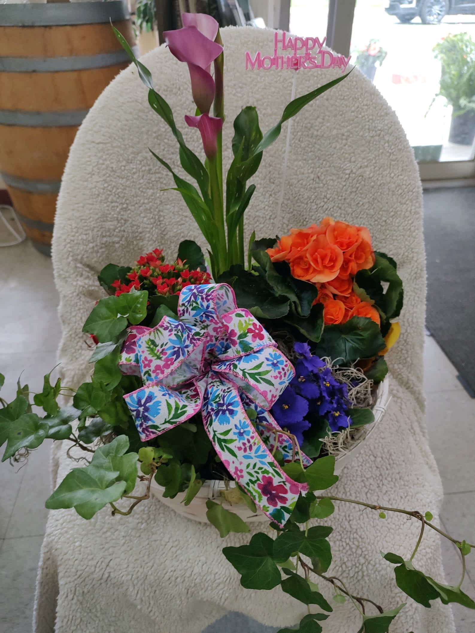 Mixed flower basket with pink calla lilies, orange blooms, and a floral ribbon