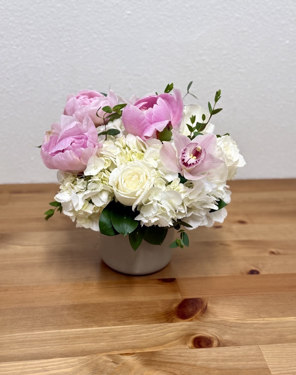 Peony Cuddles - indulge in the heartfelt gesture of honoring mothers worldwide with this meticulously crafted ceramic vase, a radiant testament to the enduring love and selflessness they embody. This beautiful arrangement features three peonies. Please note that the colors of the peonies may vary depending on market availability.