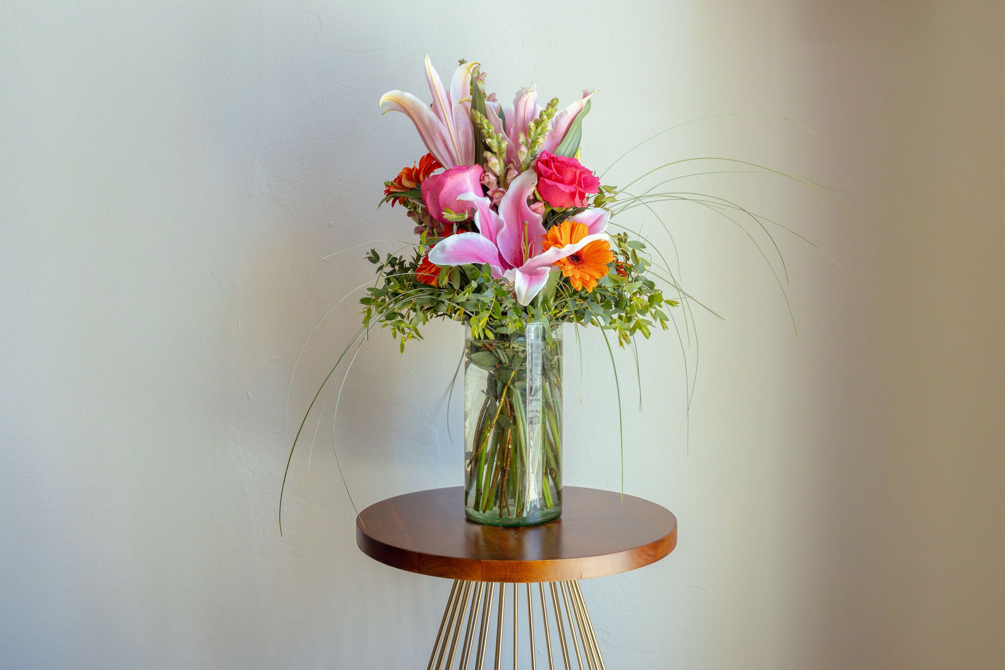 Tall bouquet of pink lilies and orange flowers in a glass vase
