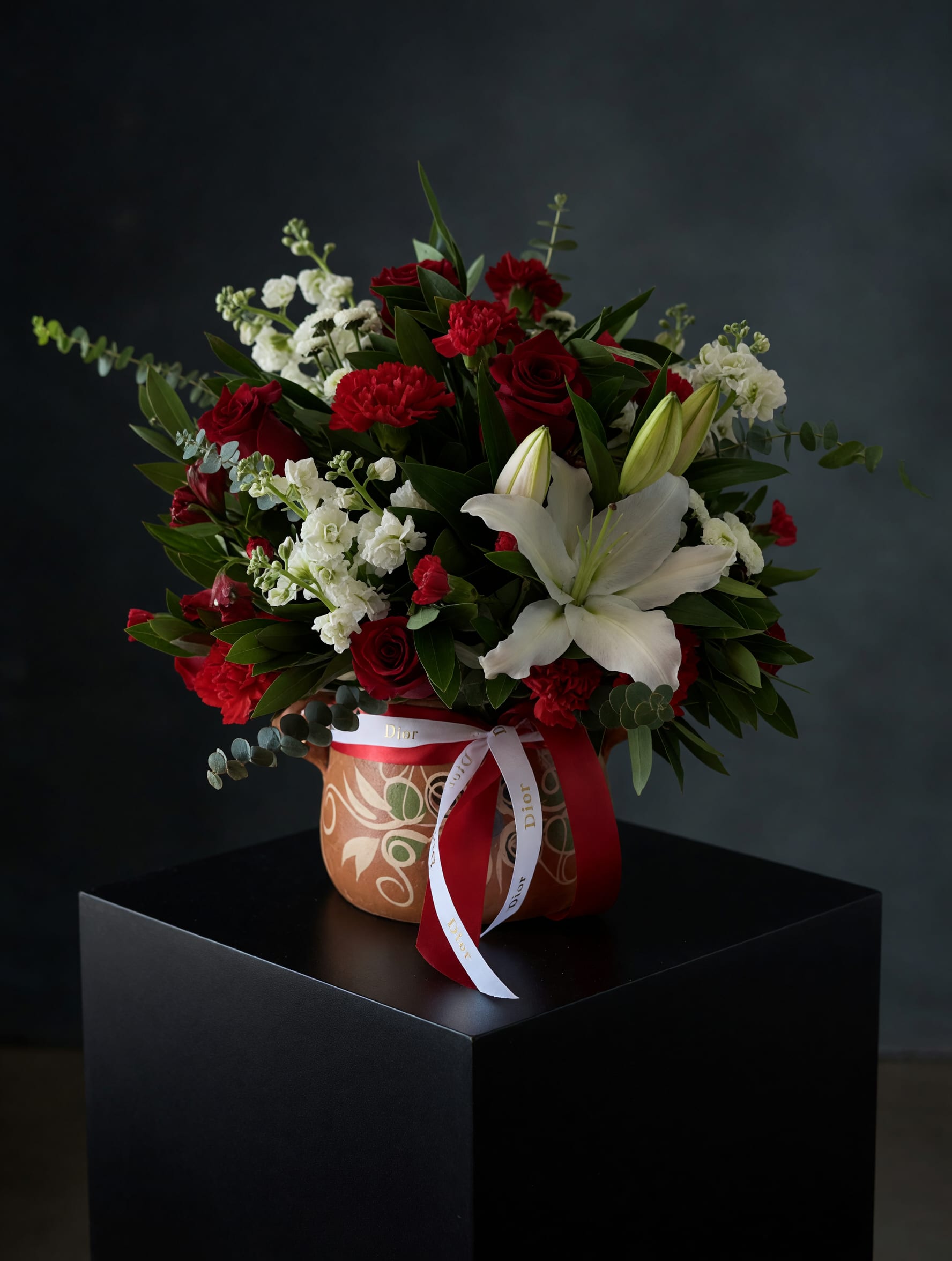 Classic Love in Clay Pot - A timeless and elegant arrangement featuring rich red roses, white lilies, and delicate accent blooms, beautifully arranged with lush greenery in a decorative clay pot (ollita de barro). Finished with a refined ribbon detail, Classic Love in Clay Pot is designed to express deep love, elegance, and heartfelt emotions.