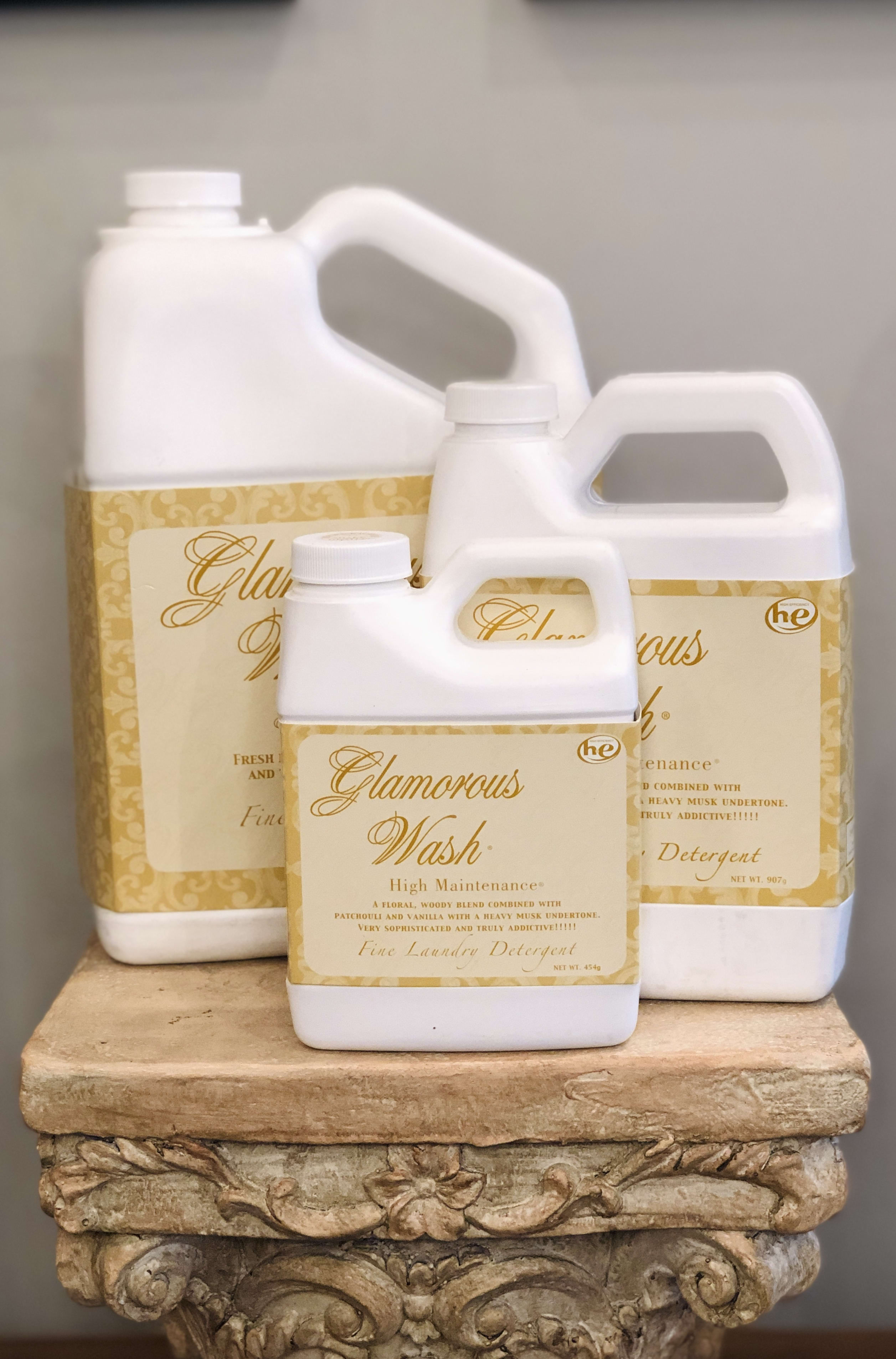 Three white laundry detergent jugs with gold labels stacked on a decorative pedestal.