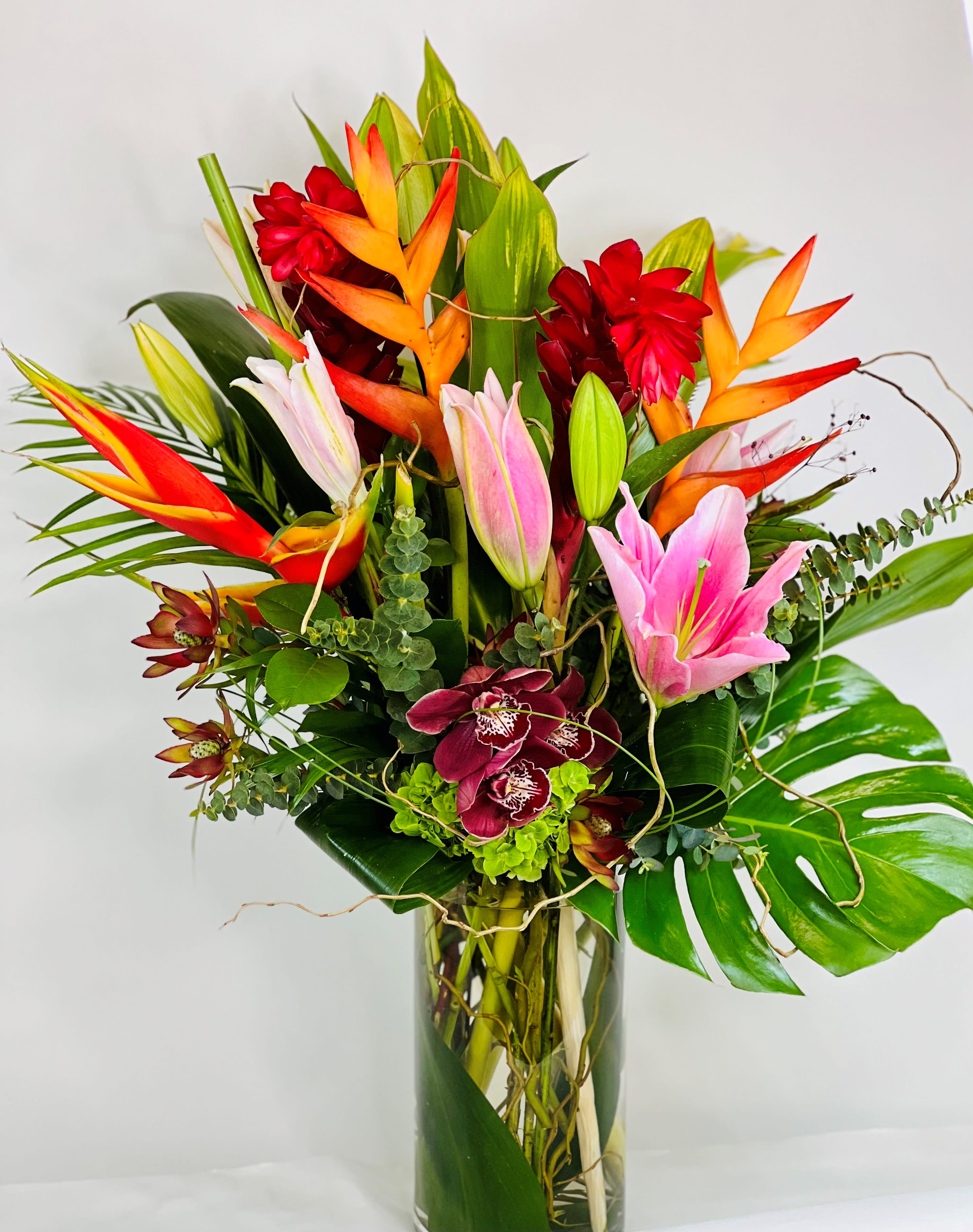 Tropical bouquet with pink lilies, orchids, and orange heliconia in a glass vase