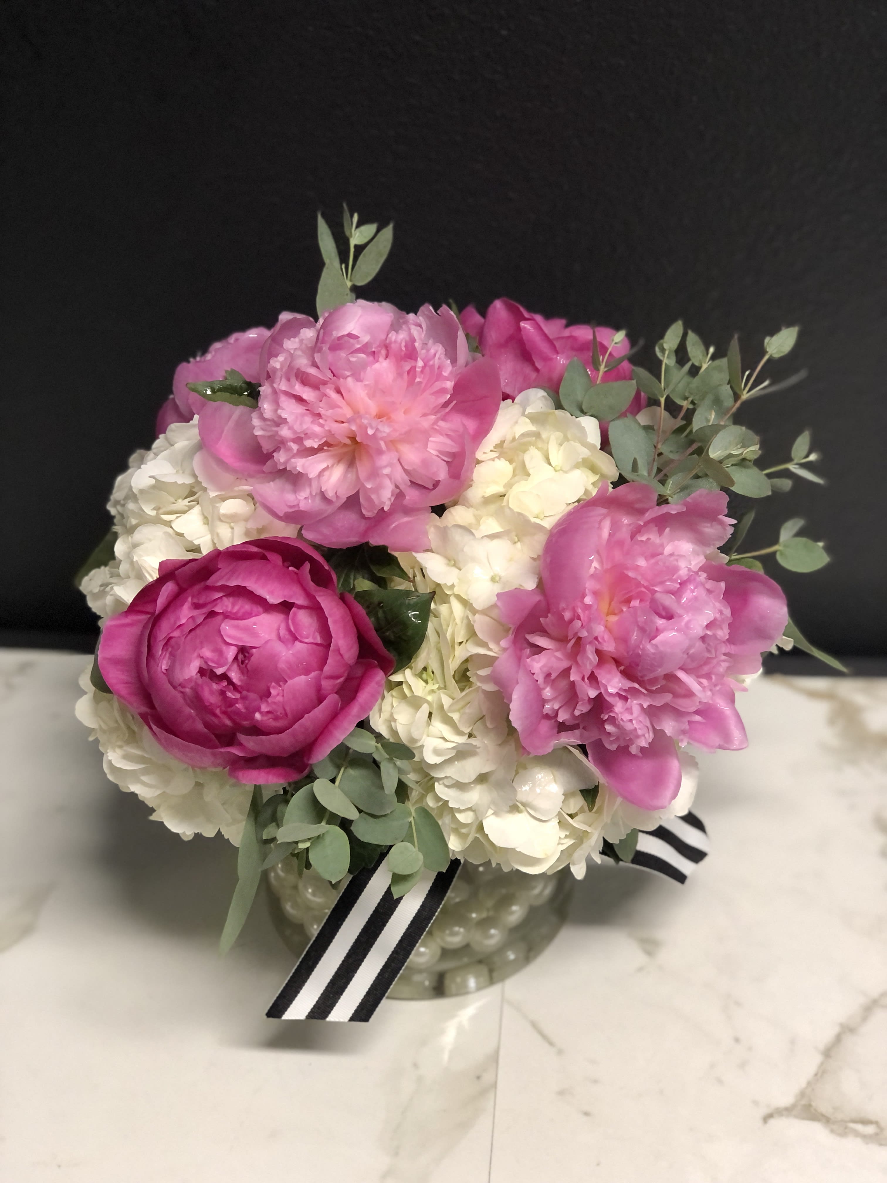 Pink peonies and white hydrangeas in a glass vase with a striped ribbon