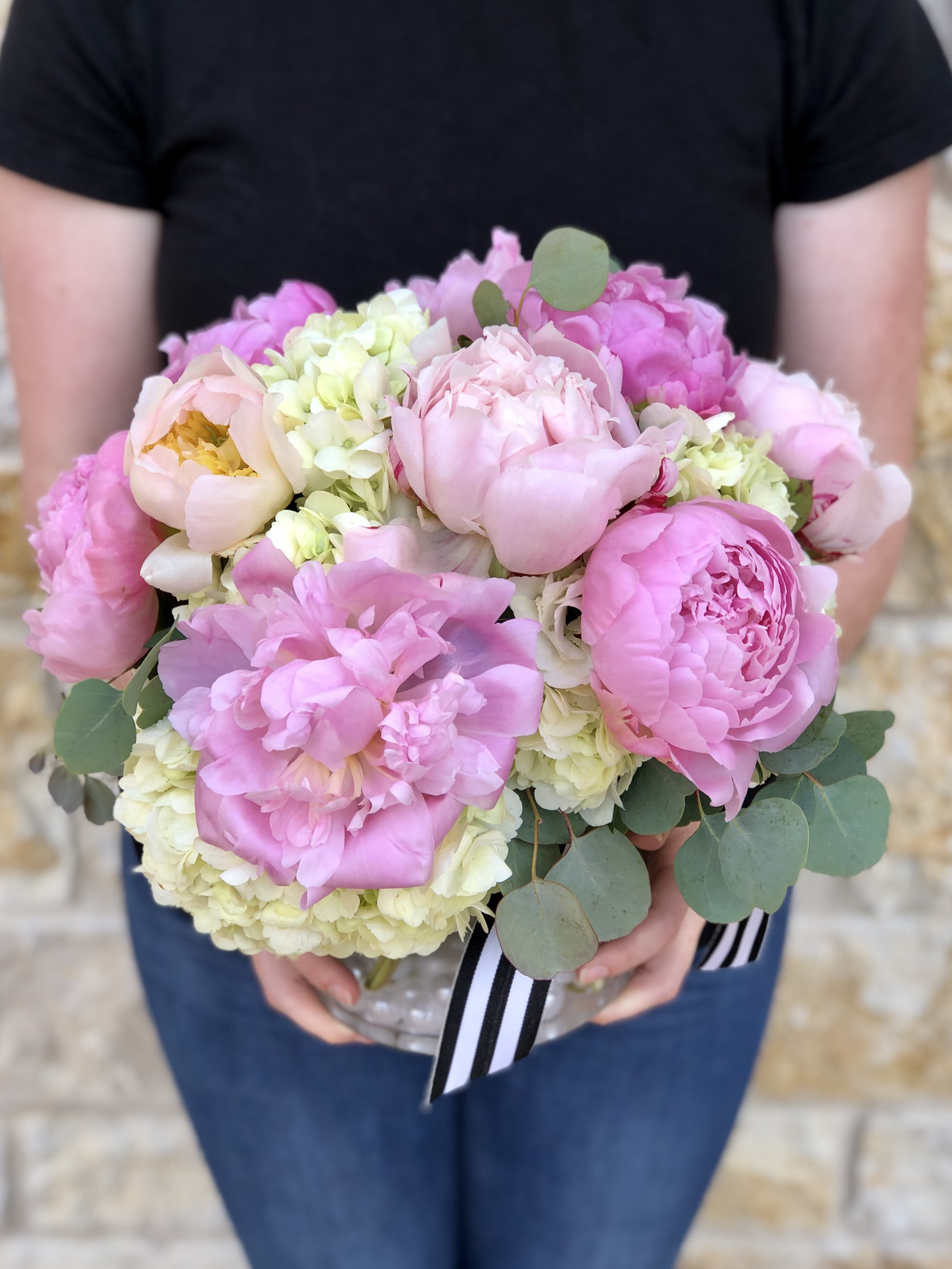 Pink peonies and pale hydrangeas in a clear vase with eucalyptus