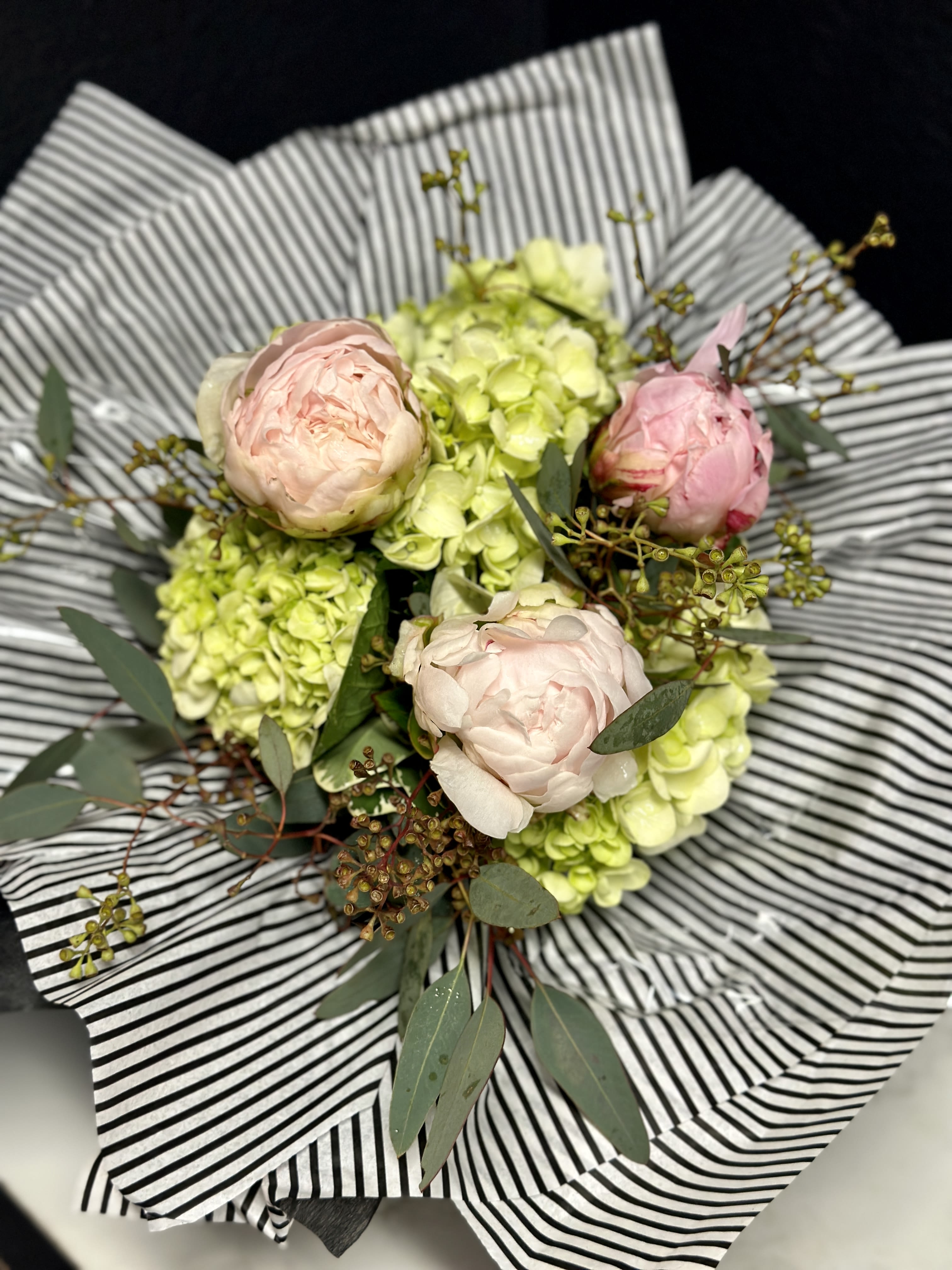 Bouquet of pale pink peonies and green hydrangeas wrapped in striped paper