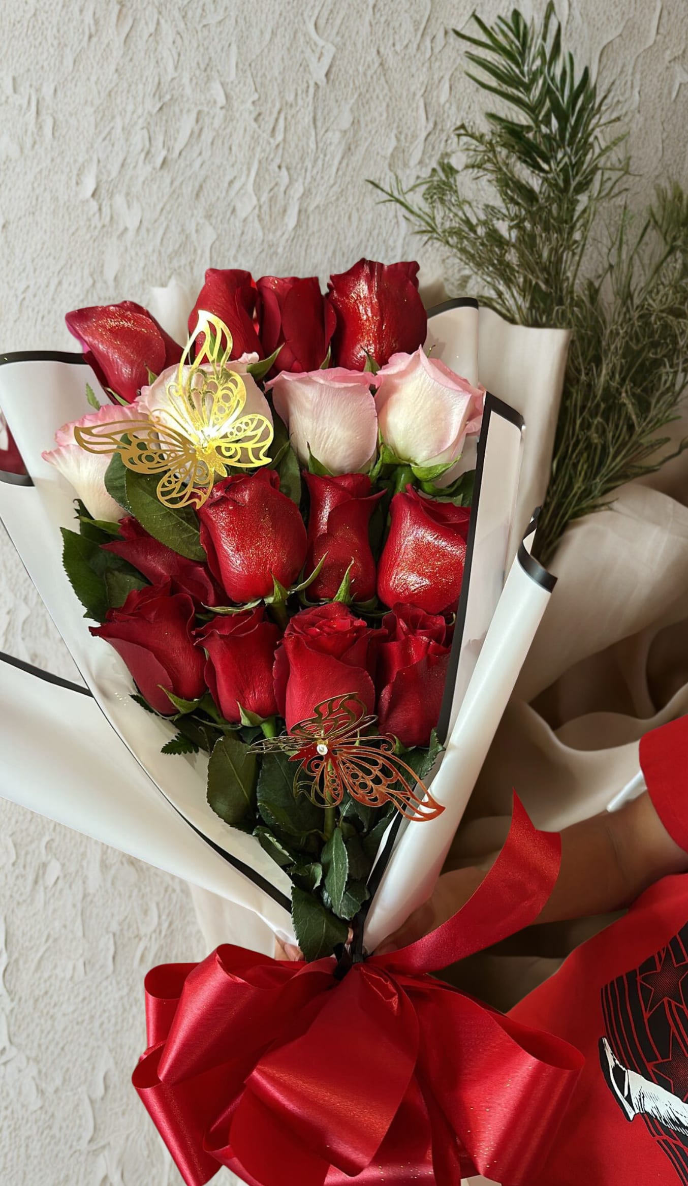 Bouquet of red and pale pink roses wrapped in white paper with a red bow