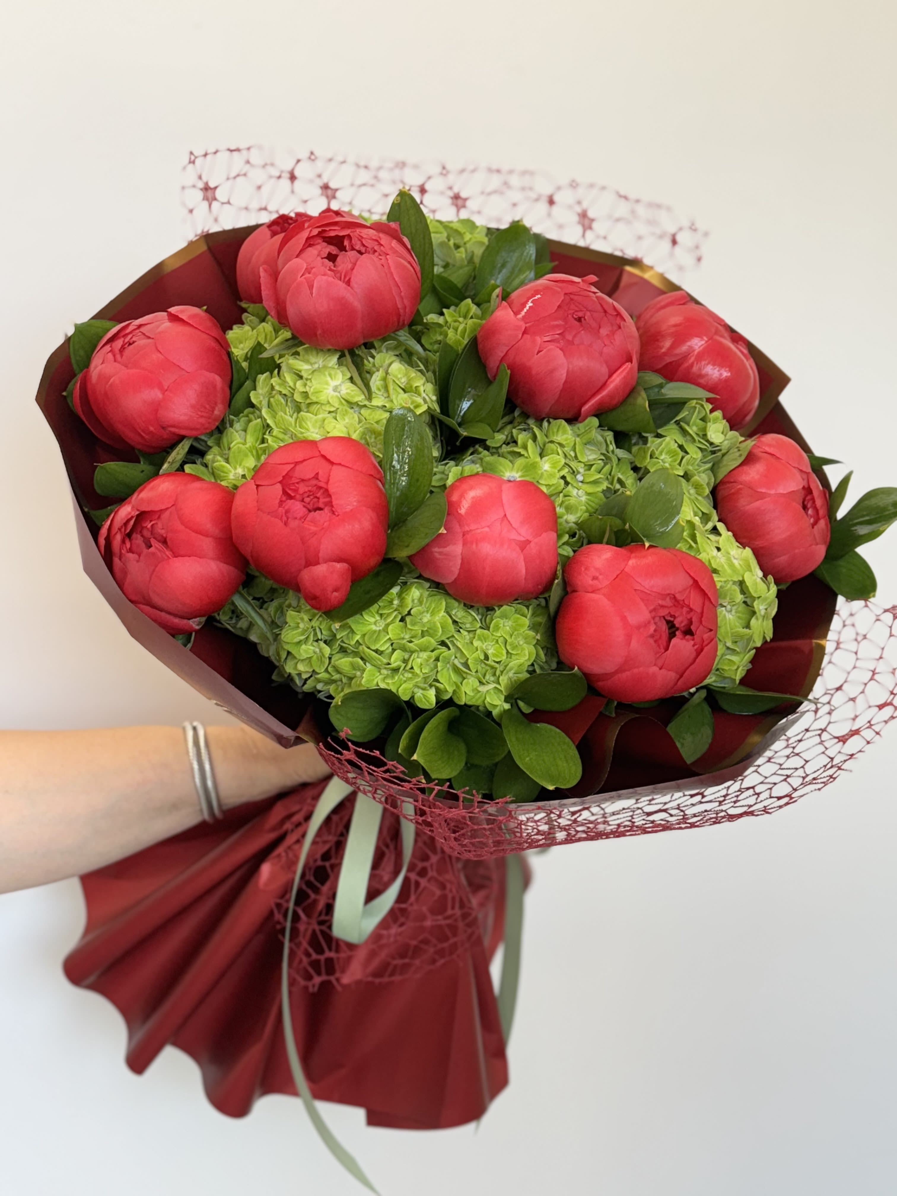 Bouquet of red peonies with green hydrangeas and burgundy wrapping