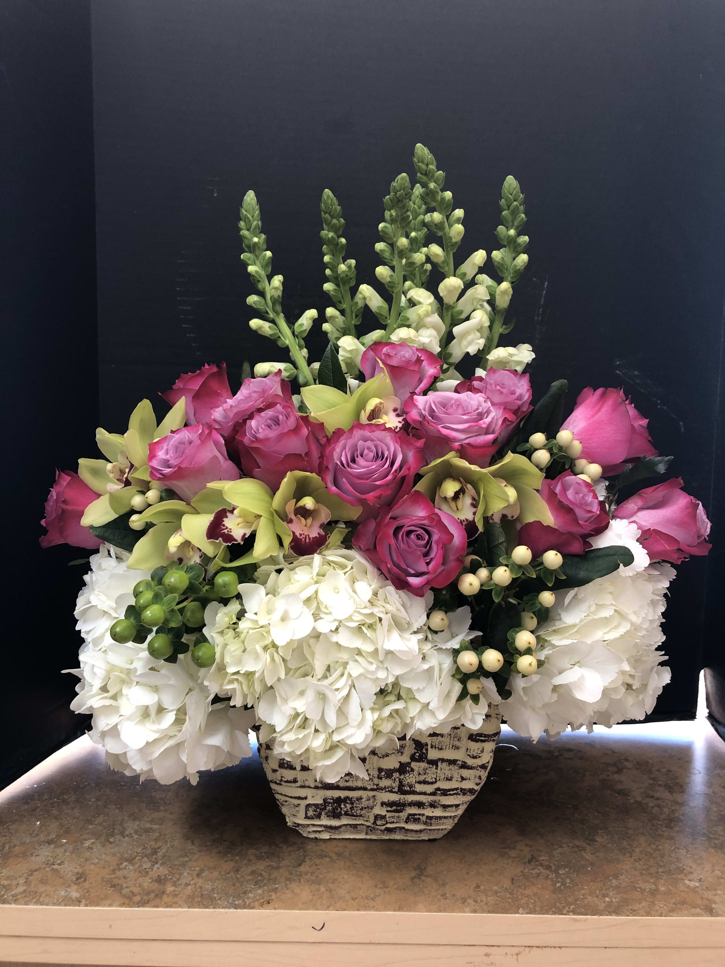 Pink roses and green orchids arranged with white hydrangeas in a patterned vase