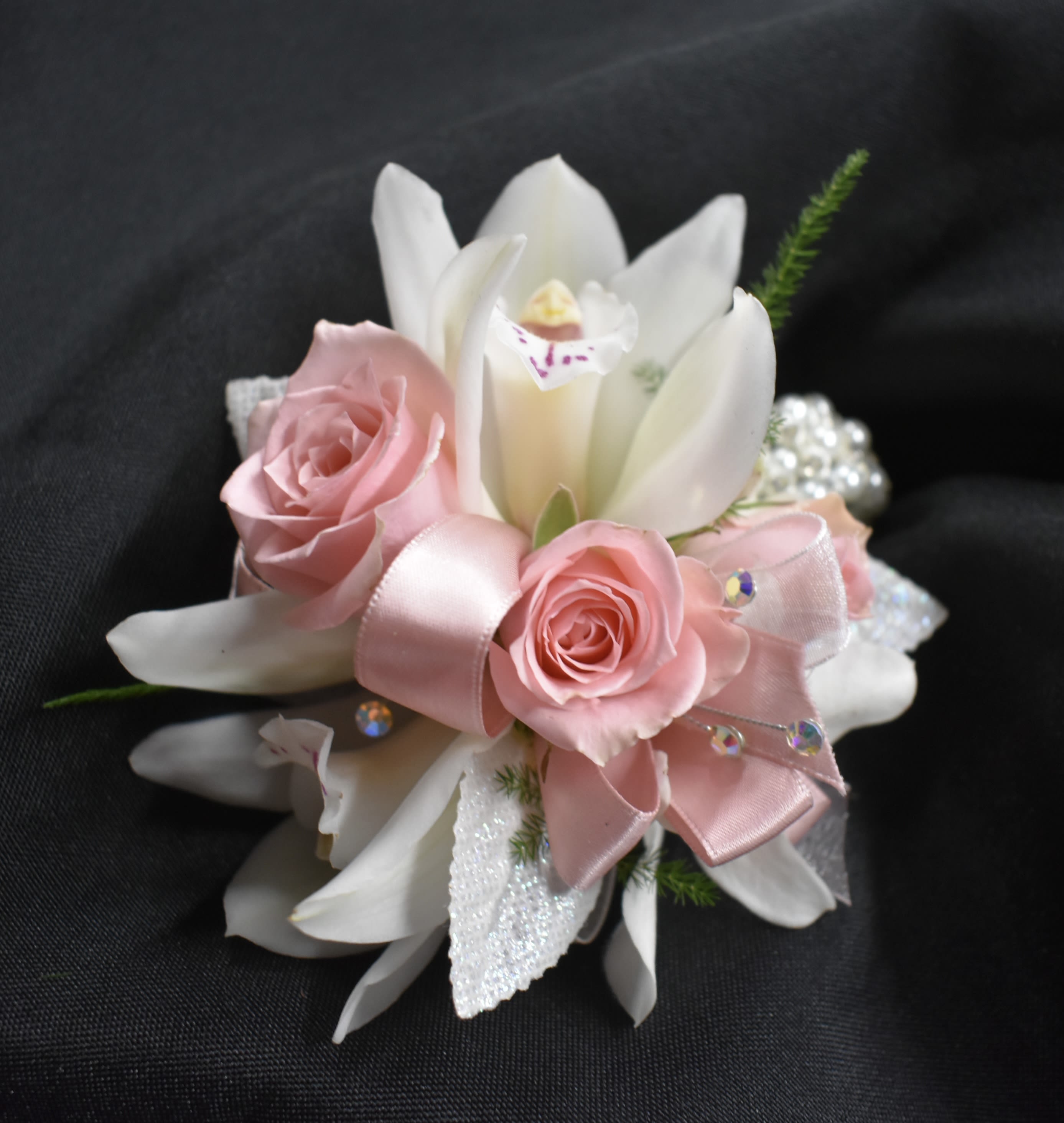 Pink roses and white lilies arranged with a pink ribbon on a dark background