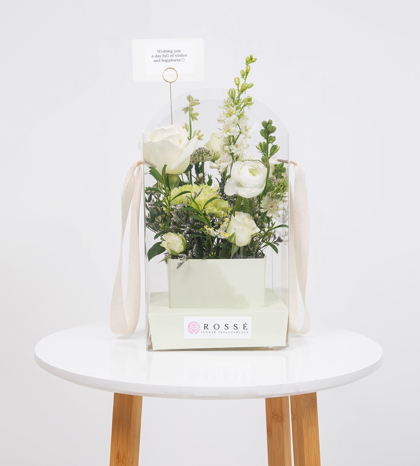 White floral arrangement in a clear gift box with a small card topper