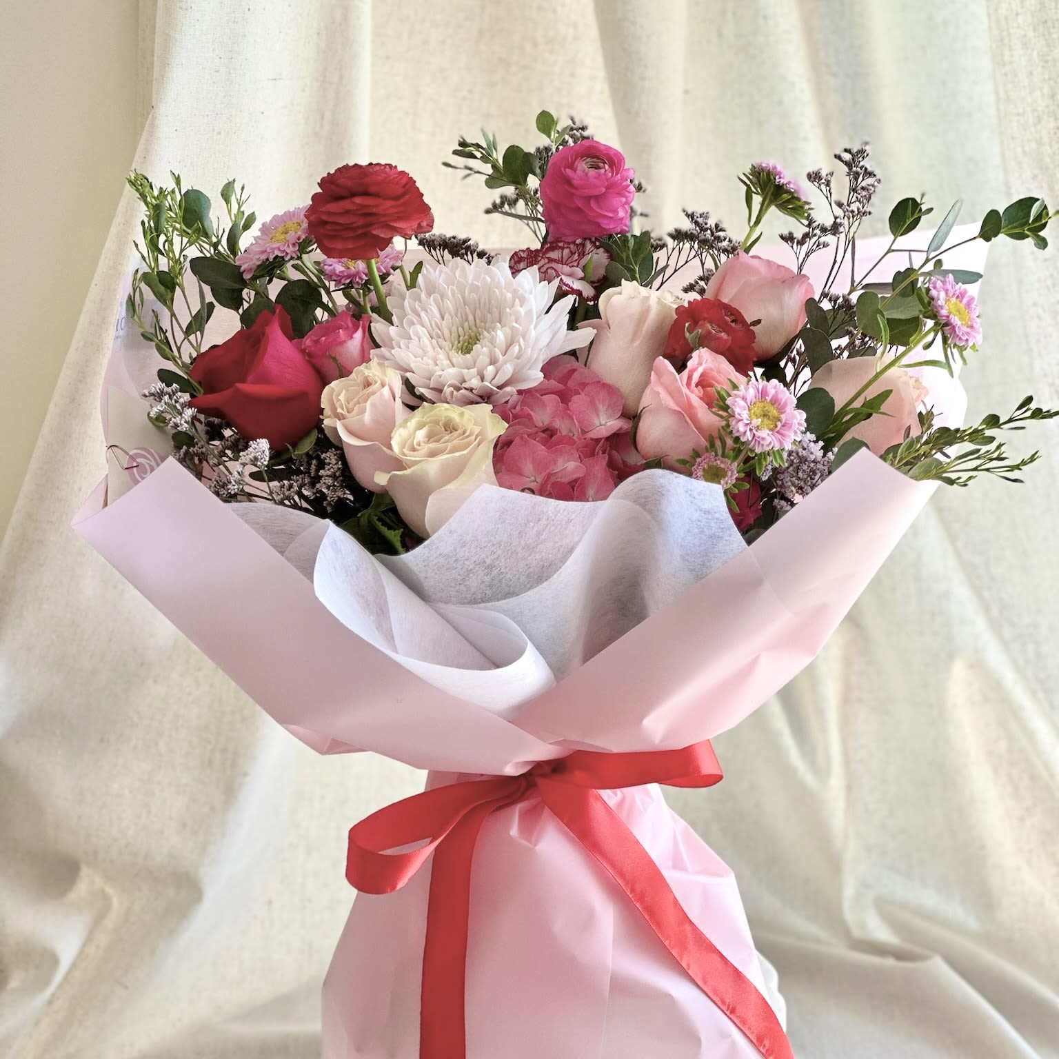 Bouquet of pink and white flowers wrapped in pale pink paper with a red ribbon