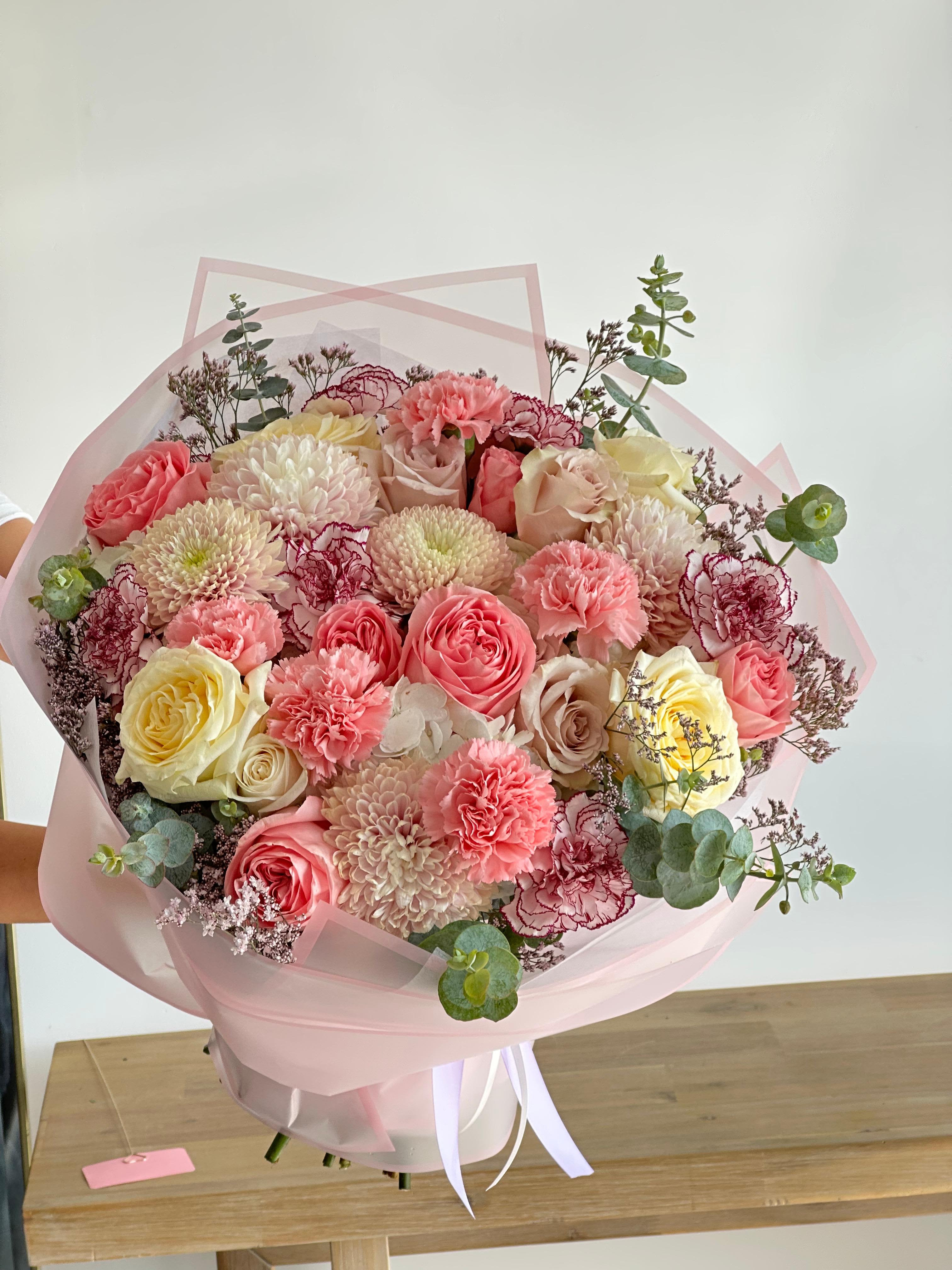 Large bouquet of pink, cream, and yellow flowers wrapped in pale pink paper