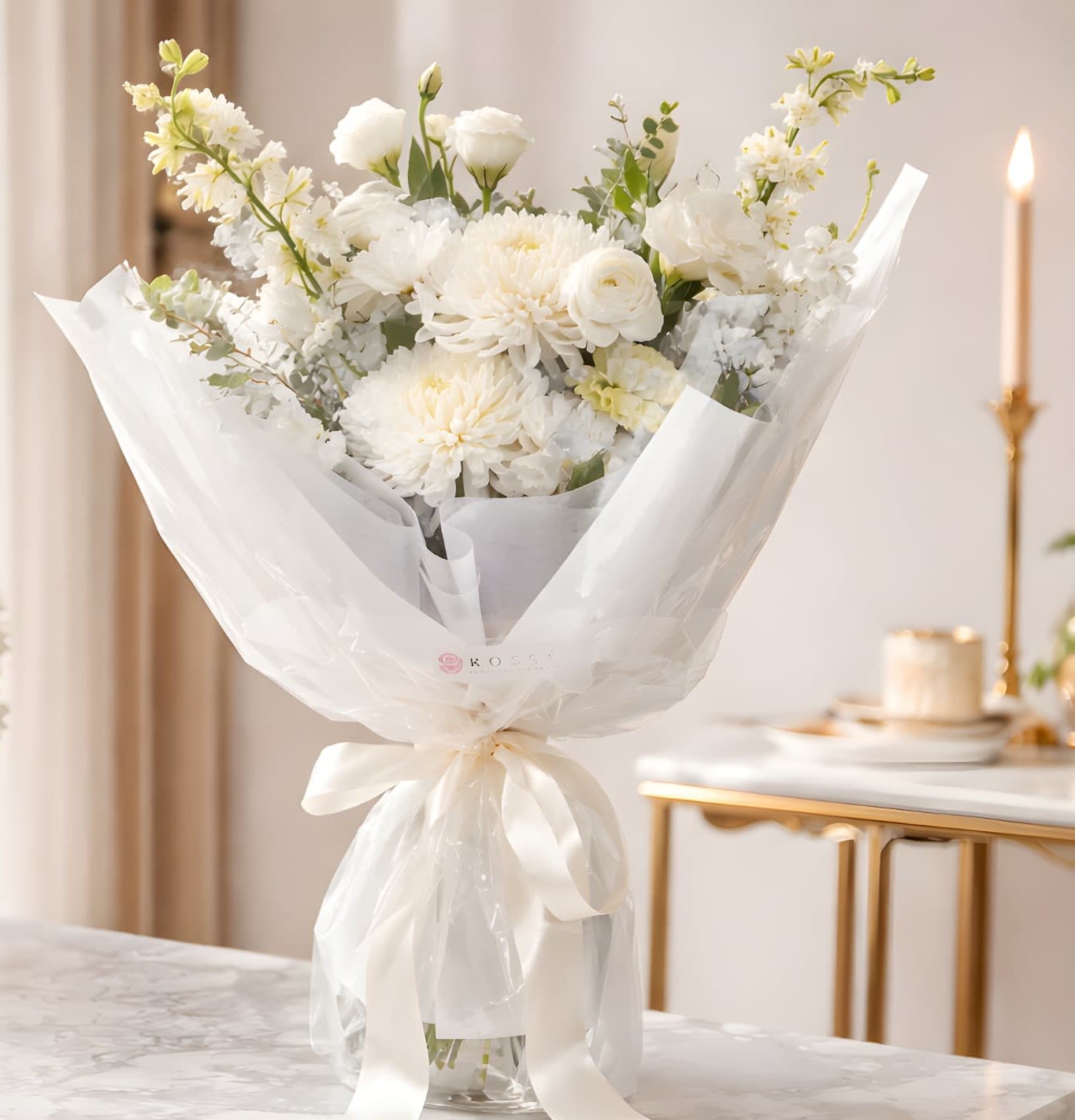 White bouquet of mixed flowers wrapped in sheer paper with a ribbon