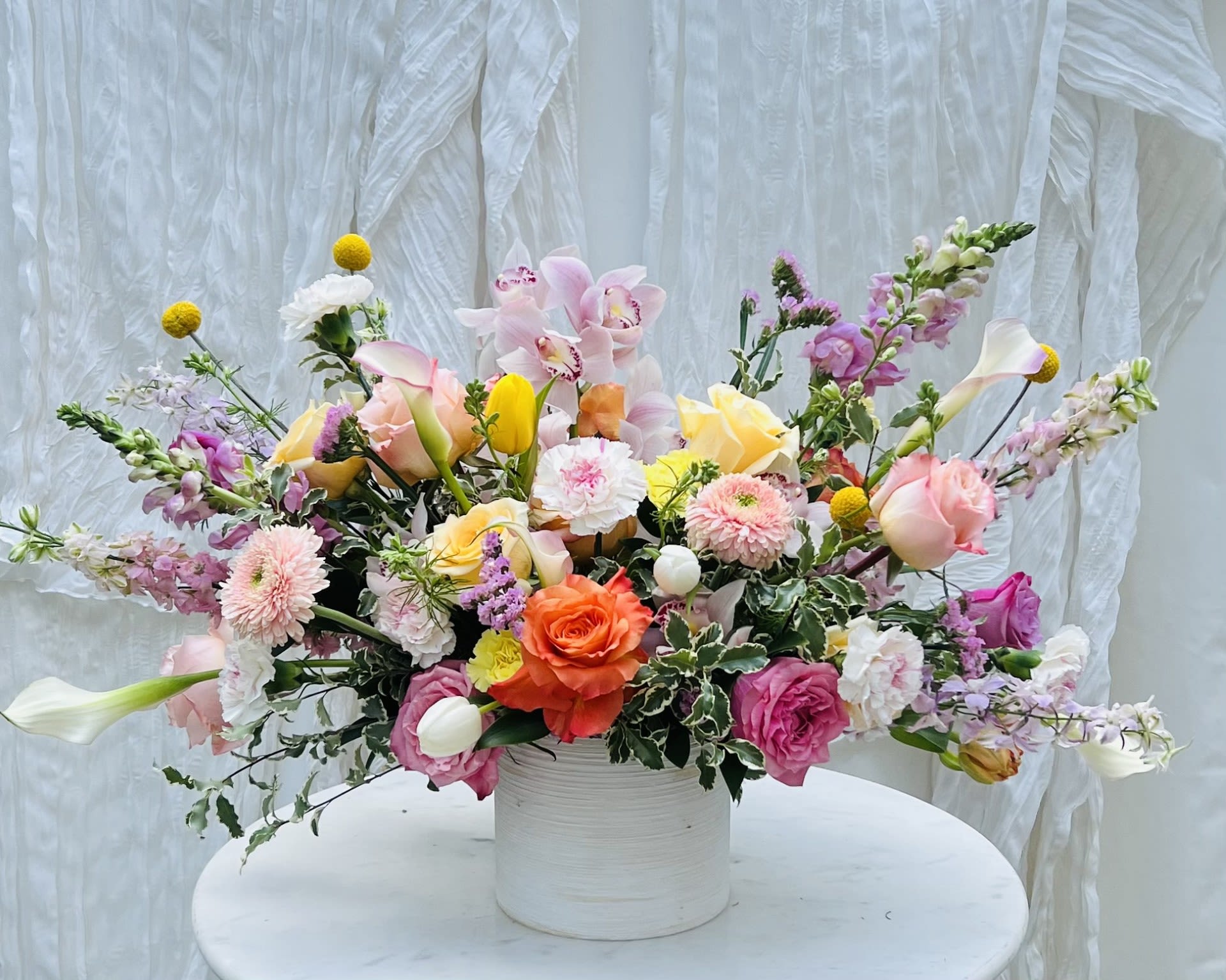 Layla - A cheerful, mixed-tone floral arrangement designed with a blend of vibrant and soft pastel blooms, complemented by lush greenery. This balanced composition brings together bold color and delicate tones, creating a look that feels fresh, lively, and effortlessly refined.  Each arrangement is handcrafted using premium seasonal flowers, thoughtfully selected for their color, texture, and natural movement. The mix of tones adds depth and visual interest, while the overall design remains cohesive and uplifting.