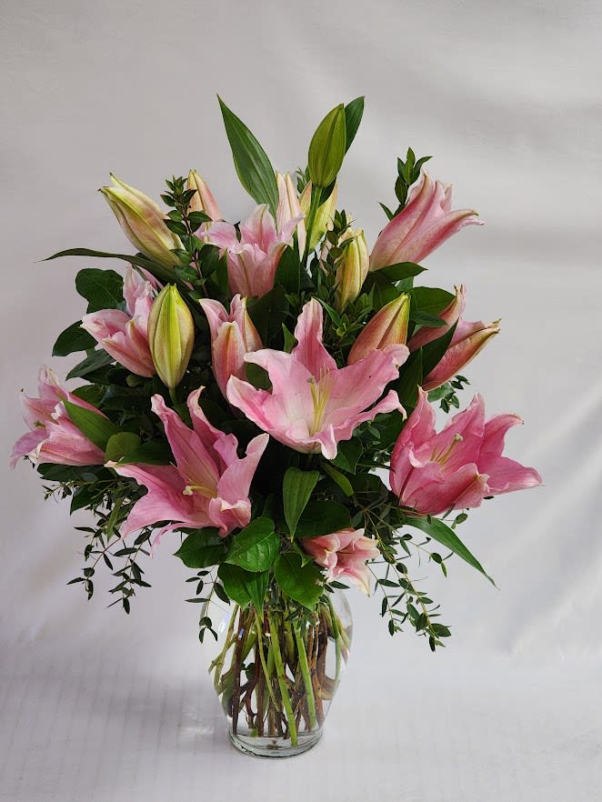 Pink lilies arranged in a clear glass vase with greenery