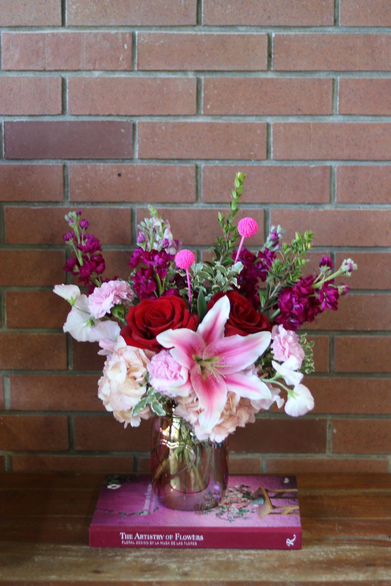 Pink and red floral arrangement in a glass vase on a book box