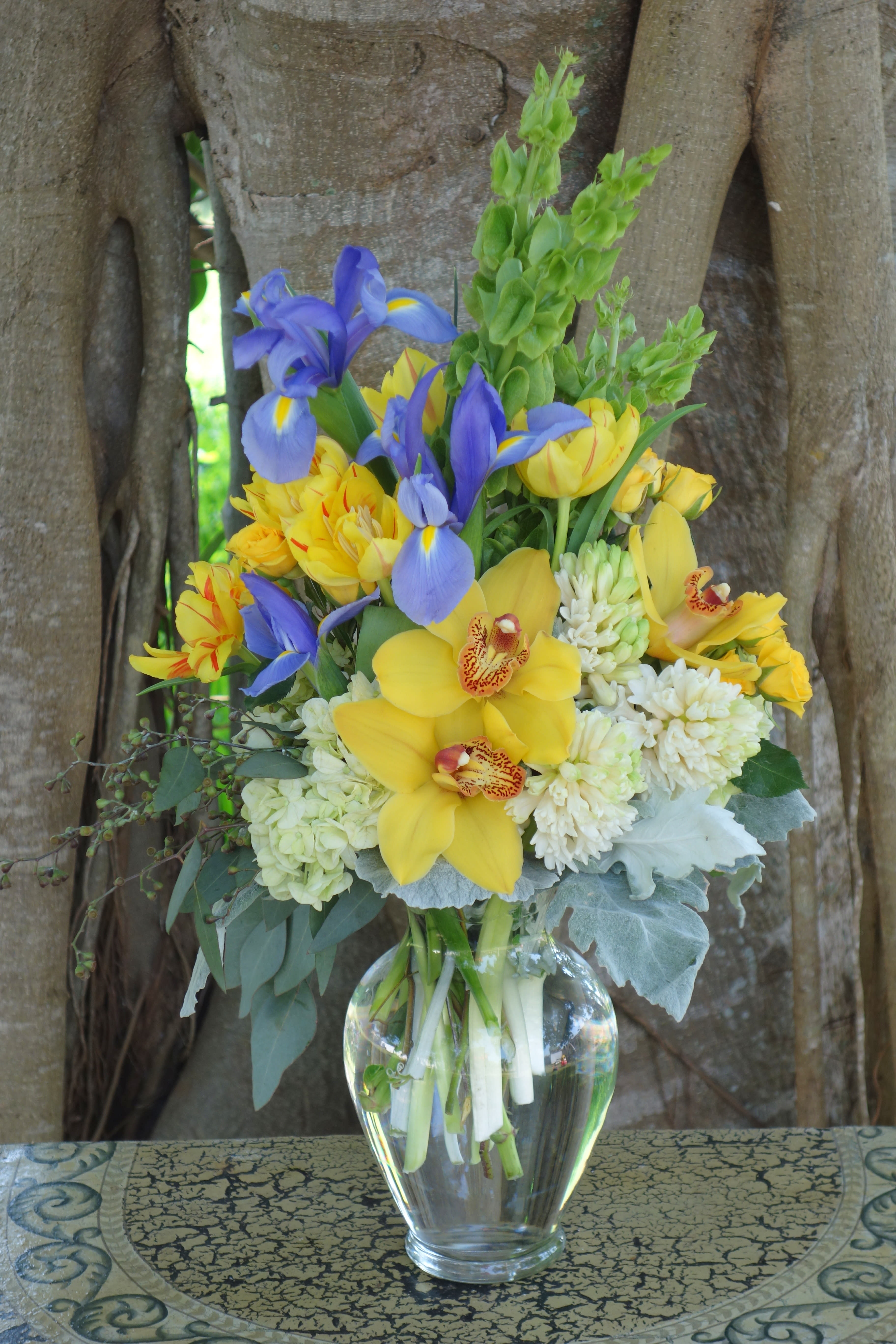 Bouquet of yellow orchids, blue irises, and white blooms in a glass vase