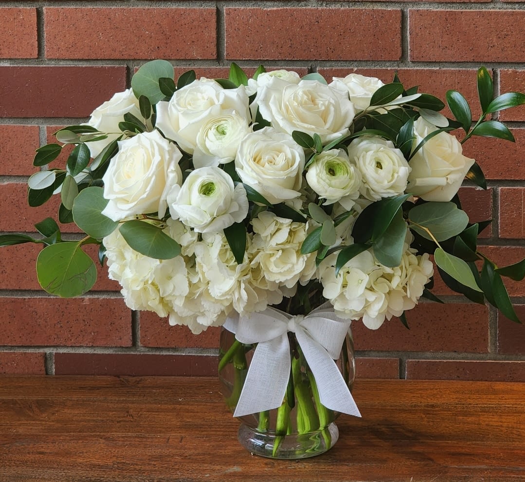 White roses and ranunculus in a glass vase with a white ribbon