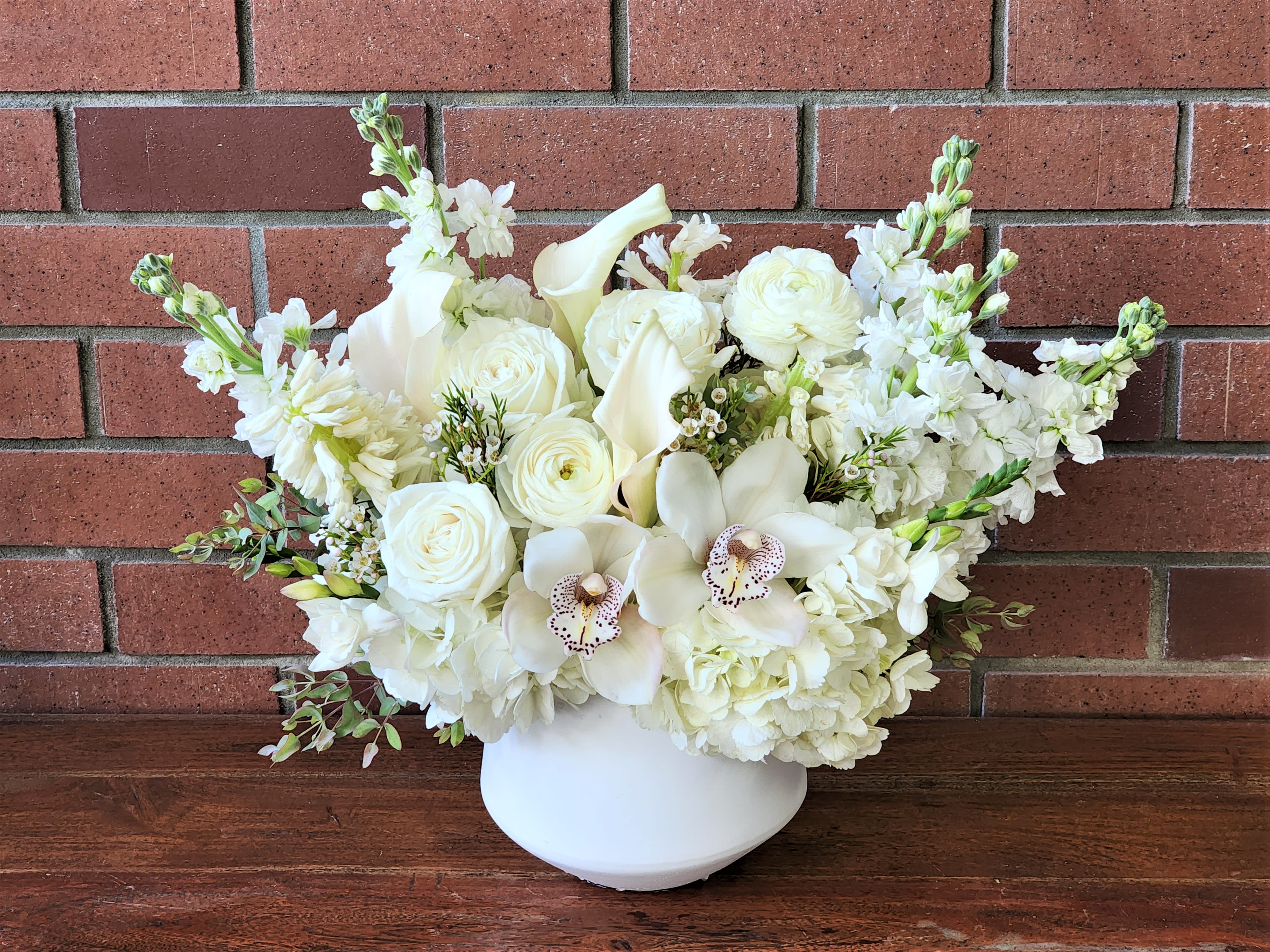 White floral arrangement in a white vase with roses and orchids