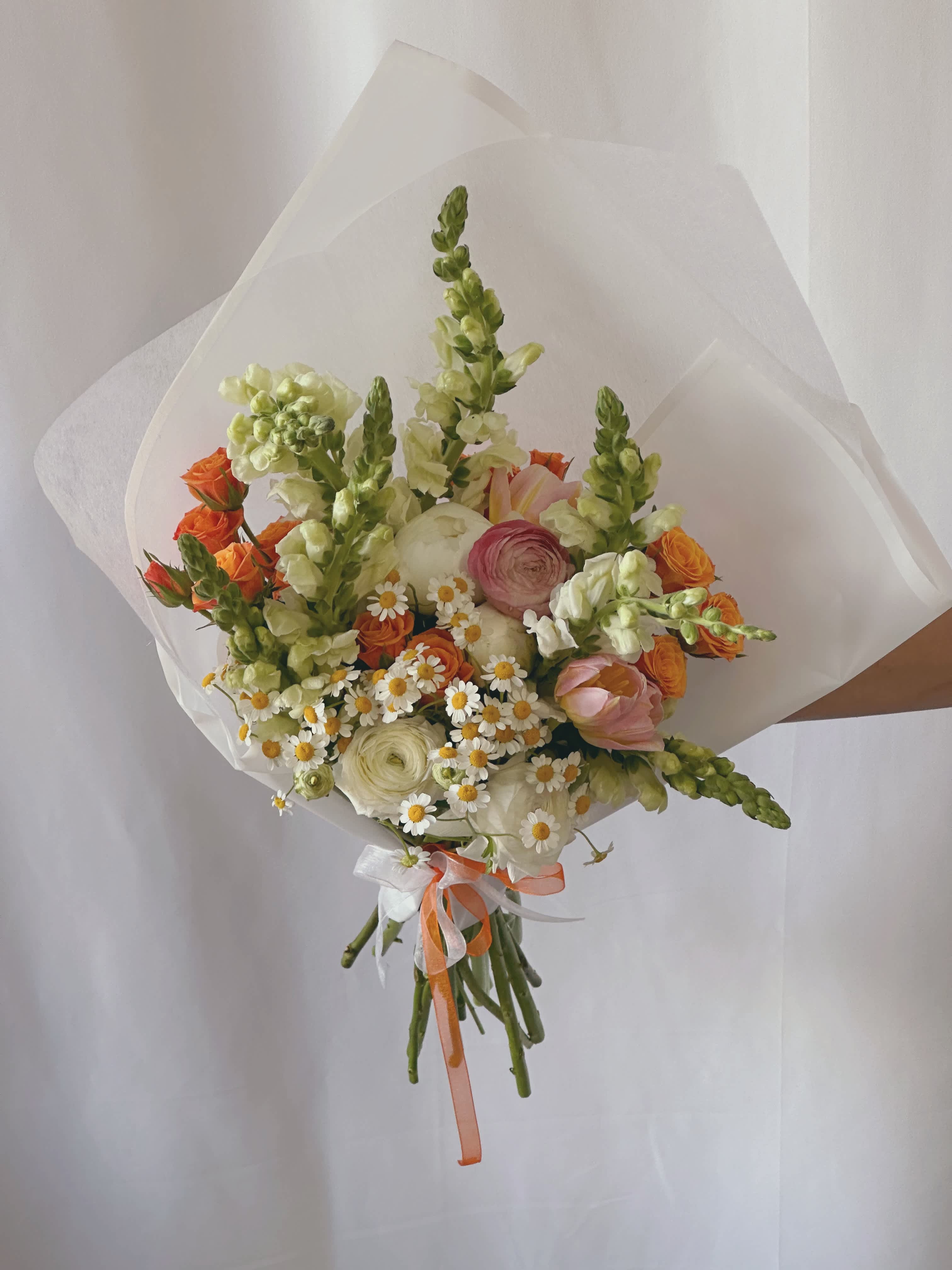 Hand-tied bouquet of orange, white, and pink flowers wrapped in white paper