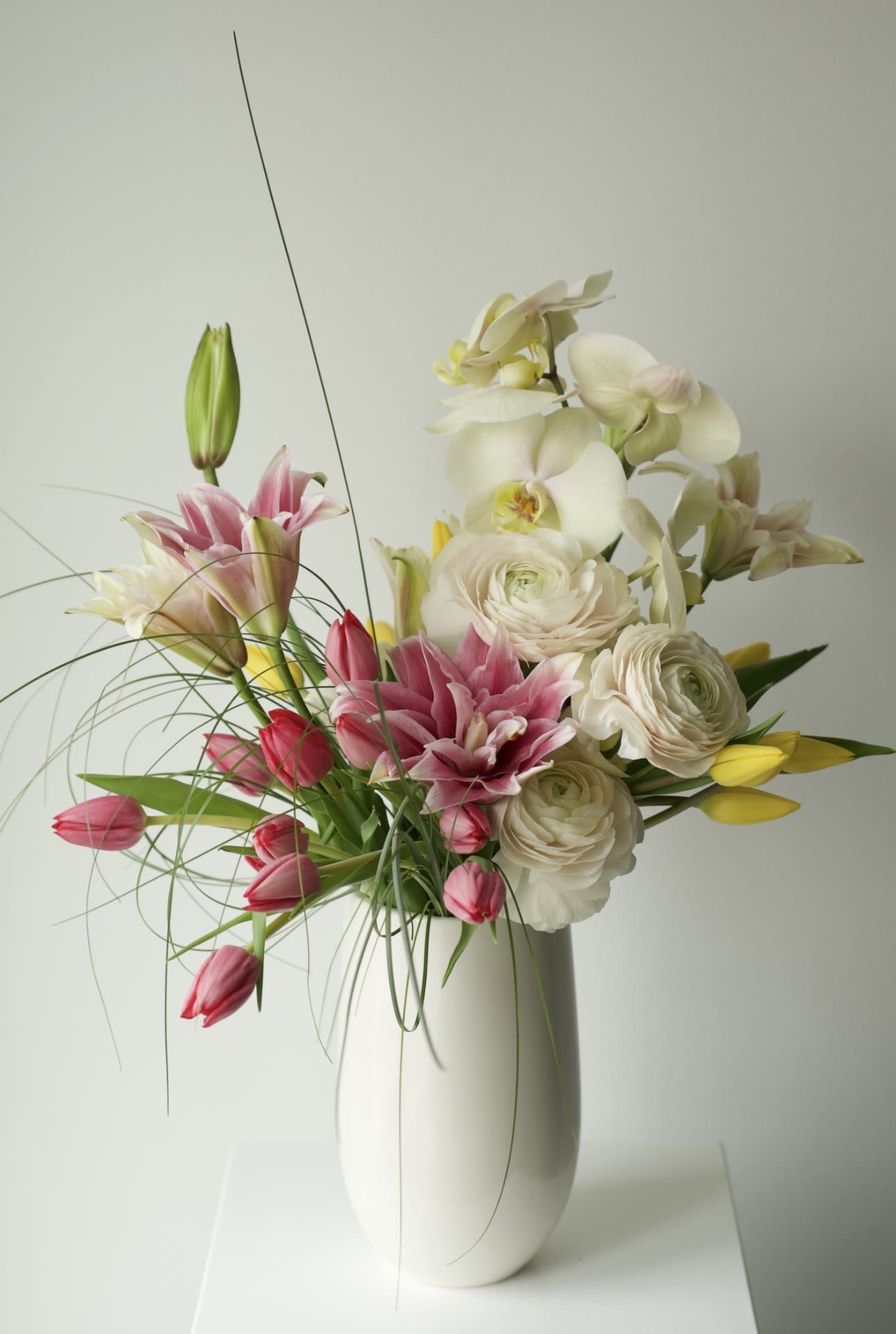 Pink Silk Bloom - A modern garden-style arrangement featuring delicate pink lilies, premium white ranunculus, soft tulips, and elegant phalaenopsis orchids arranged in a sculptural silhouette.   Designed with movement, texture, and a refined spring palette, this composition brings an elevated editorial feel to any space.   Perfect for birthdays, celebrations, thank you gifts, or simply adding beauty to everyday moments. 