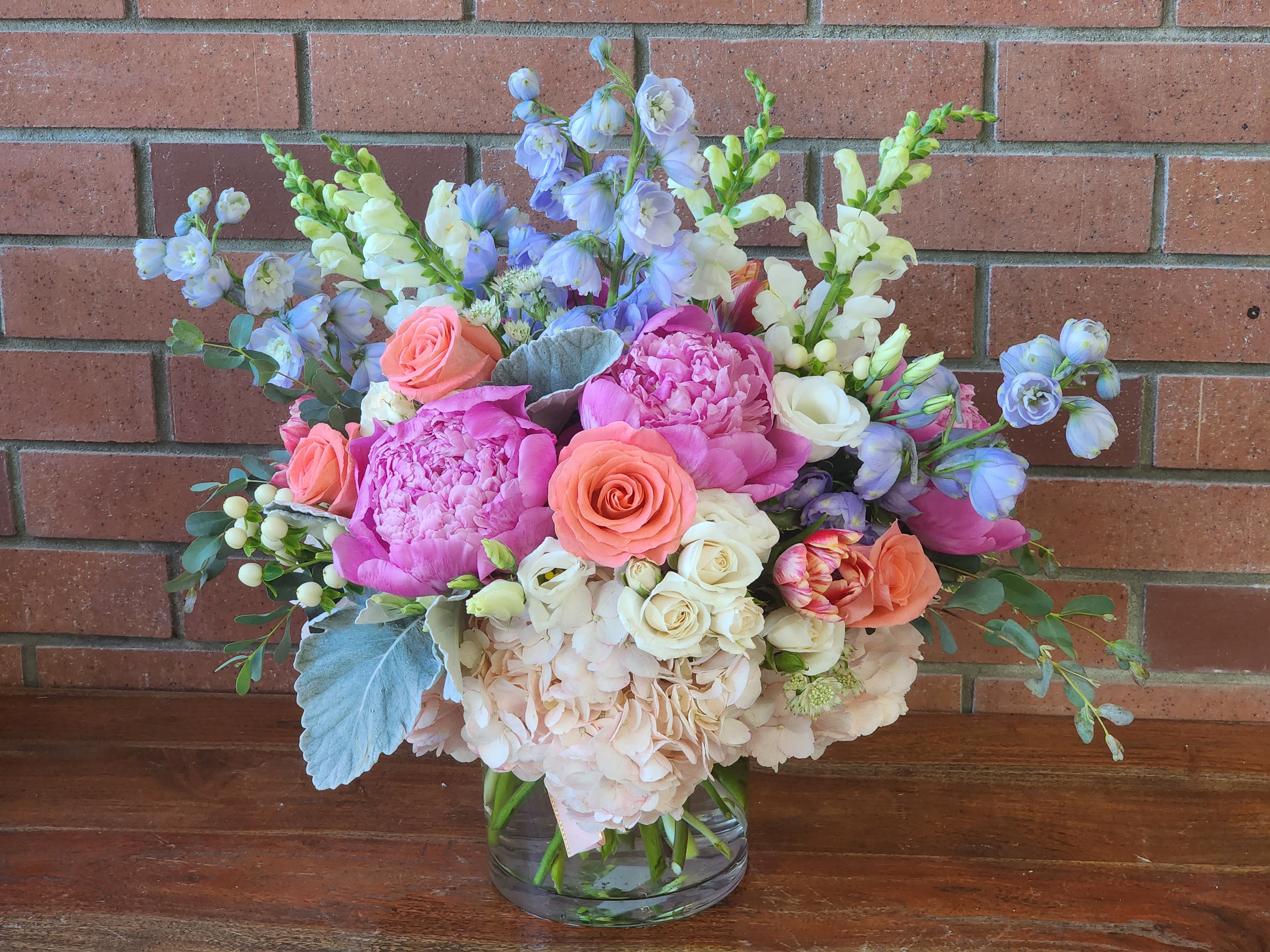 Mixed bouquet of pink, peach, white, and blue flowers in a glass vase