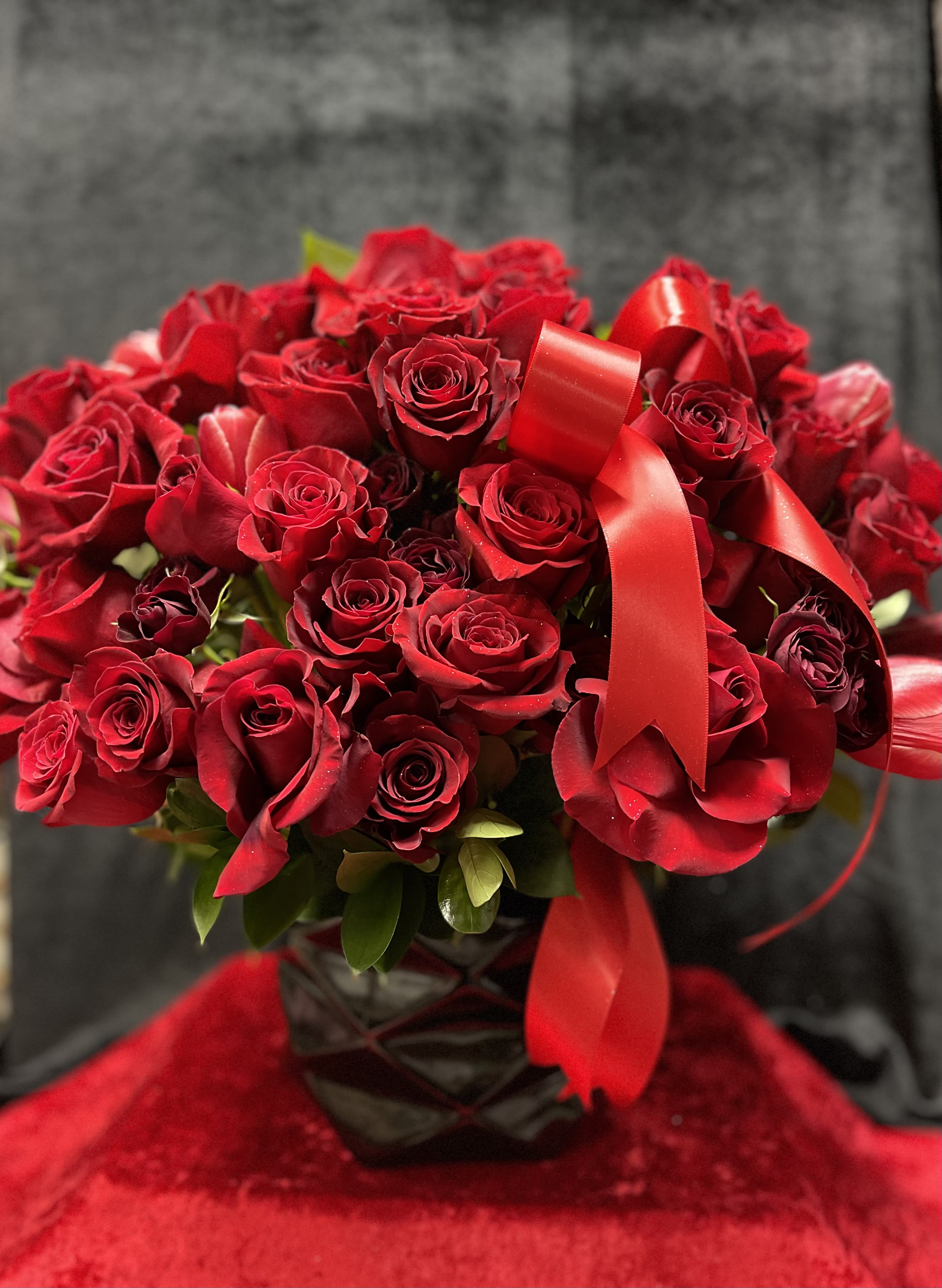 Bouquet of red roses with a red ribbon in a dark vase