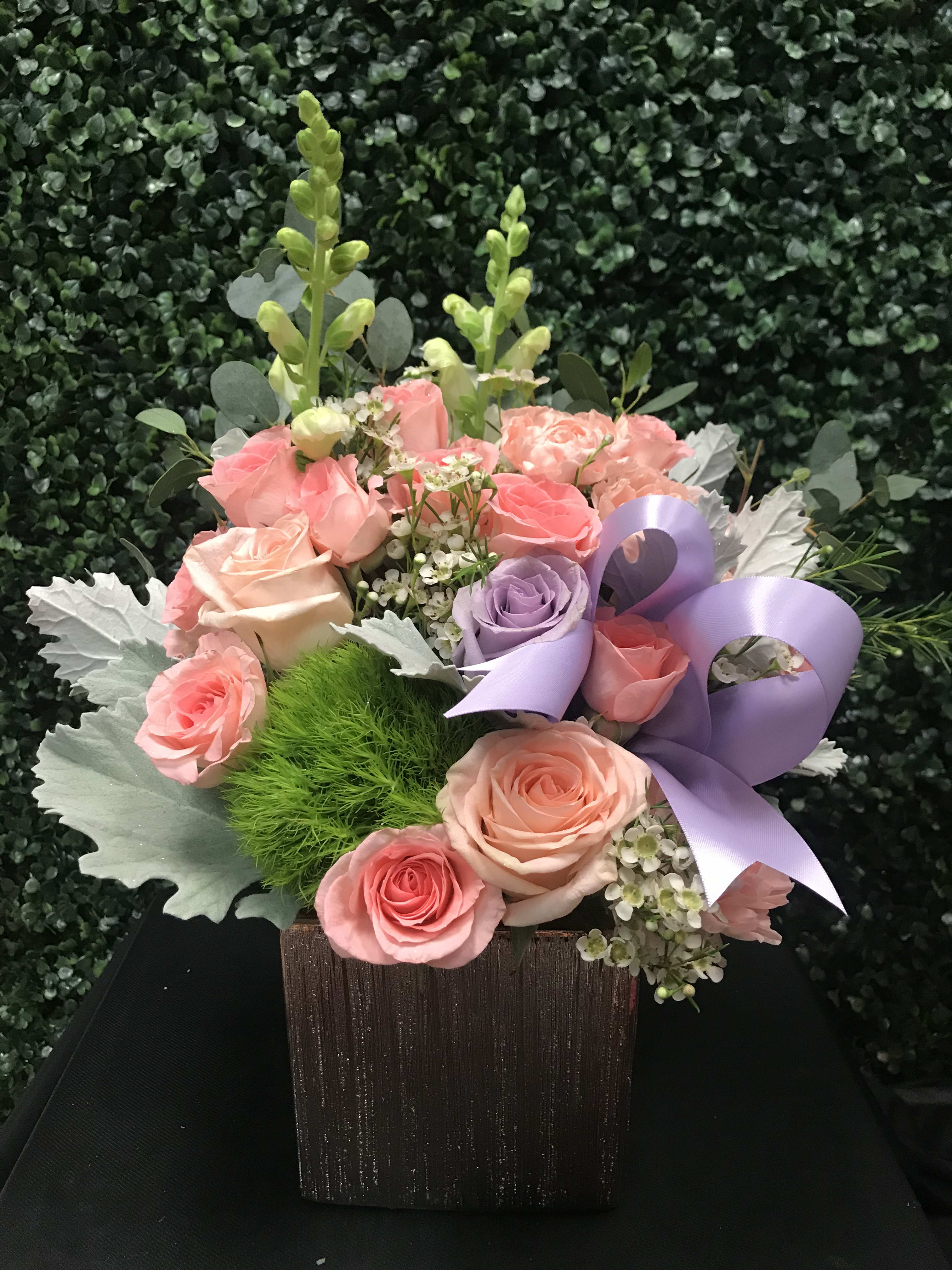 Pink and lavender roses in a square wooden box with a purple ribbon