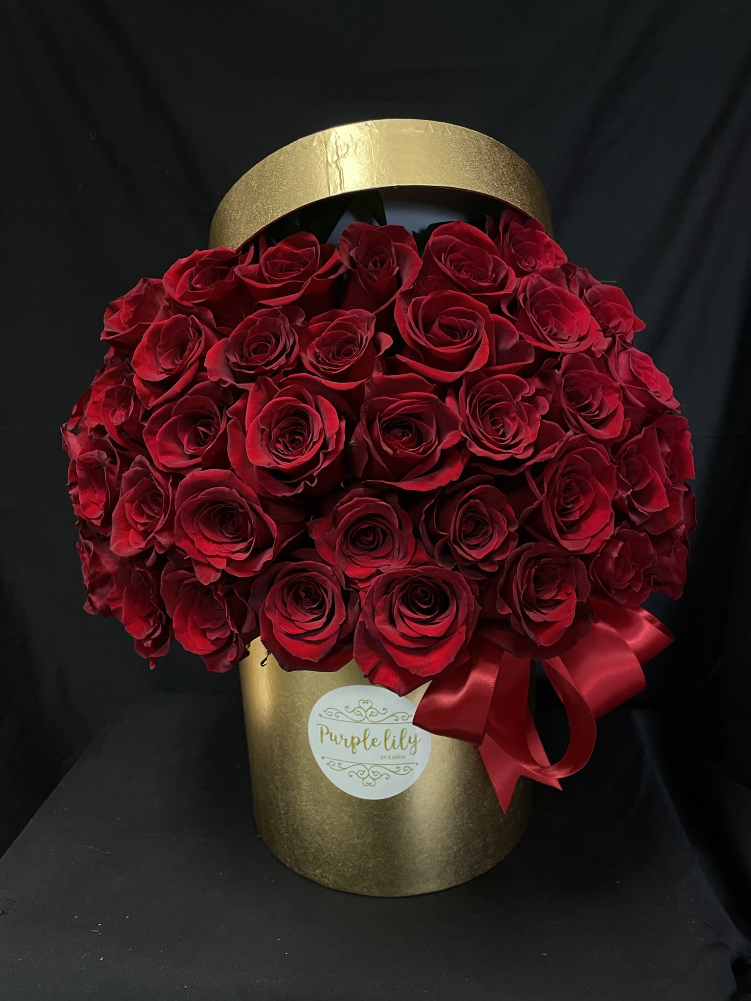 Red roses arranged in a gold hatbox with a red ribbon
