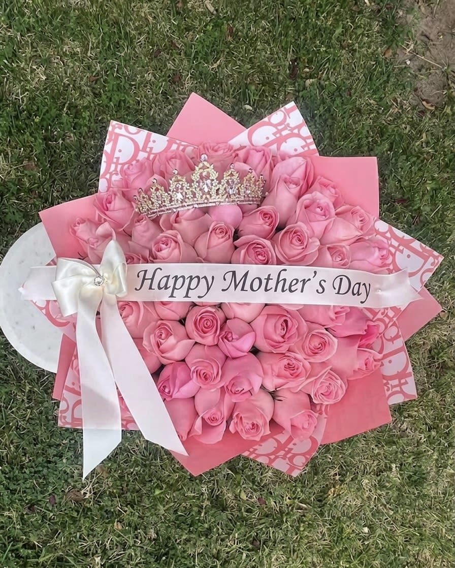 Mother’s Day Rose Bouquet  - Celebrate the woman who wears the crown with this stunning, hand-crafted bouquet 50 roses count Featuring a lush collection of premium pink roses arranged in a dense, heart-like formation, this display is accented by a shimmering crystal tiara and a signature "Happy Mother’s Day" satin banner. The arrangement is elegantly wrapped in high-fashion inspired pink and white patterned paper, finished with a crisp white bow—making it the perfect tribute for a queen. This standout piece is designed to bring a touch of luxury and heartfelt appreciation to her special day.