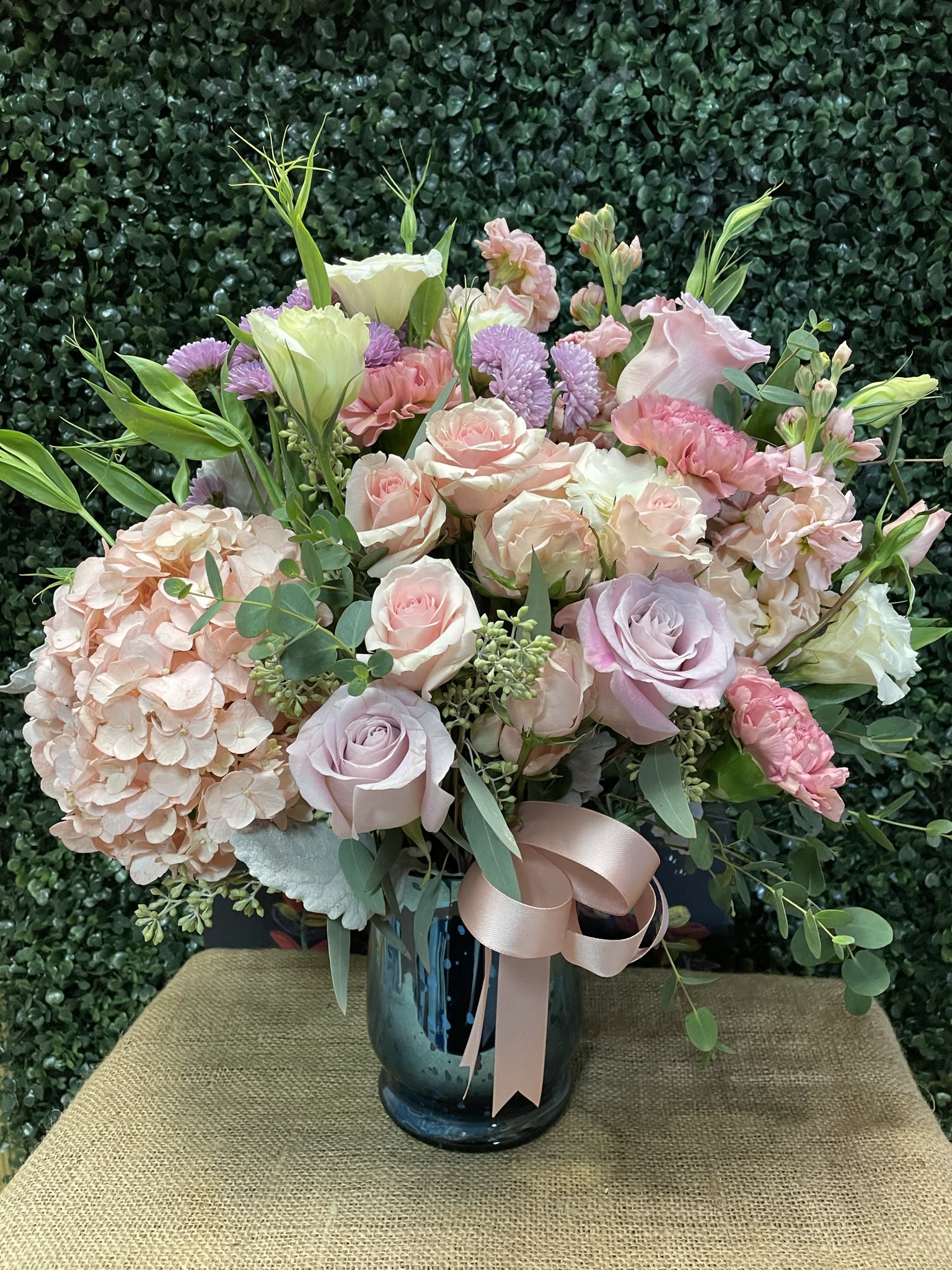 Pastel bouquet of roses, hydrangea, and lisianthus in a blue vase with ribbon