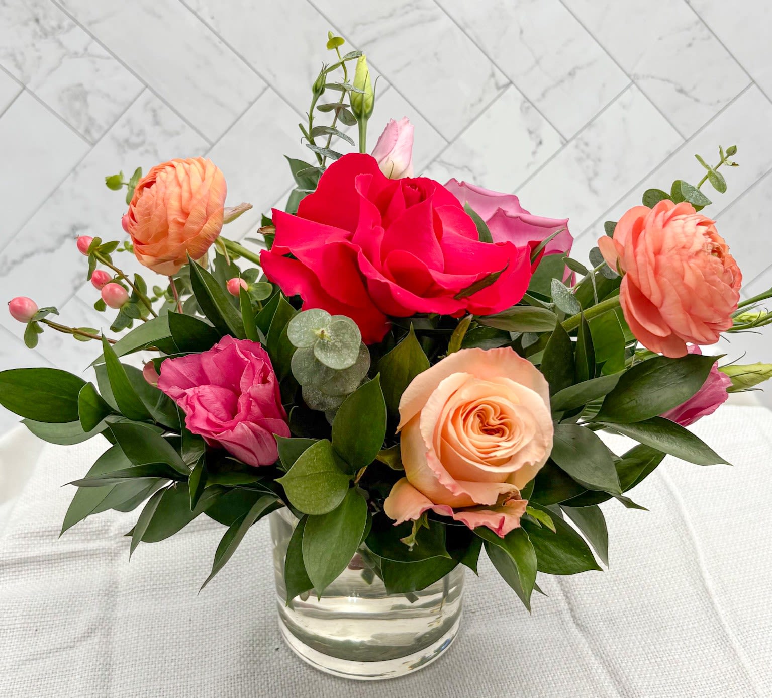 COSMOPOLITAN MOM-TINI - Part of our Mother's Day "Mom-Tini Collection", the Cosmopolitan Mom-Tini is the perfect arrangement to gift the Cosmo Martini lover in your life. This arrangement is full of Peach &amp; Pink roses, Peach Ranunculus, Lisianthus, Berries, Eucalyptus &amp; upscale greenery. Add a little something extra, gourmet chocolates, hand poured candles. See all our gift selections under the thoughtful gifts tab. Or call the shop and let us know what you are looking for and we will do the shopping for you.