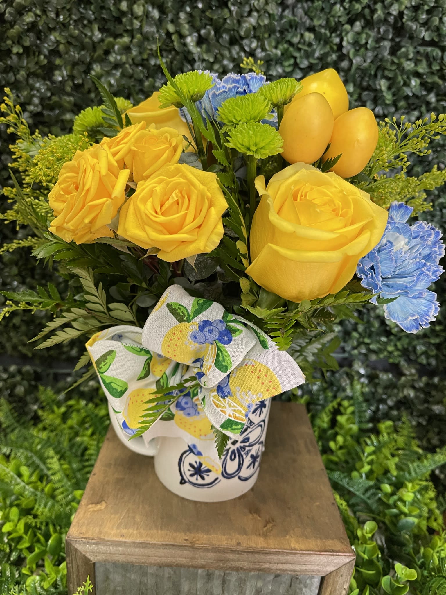 Yellow roses and blue carnations in a patterned mug with a bow