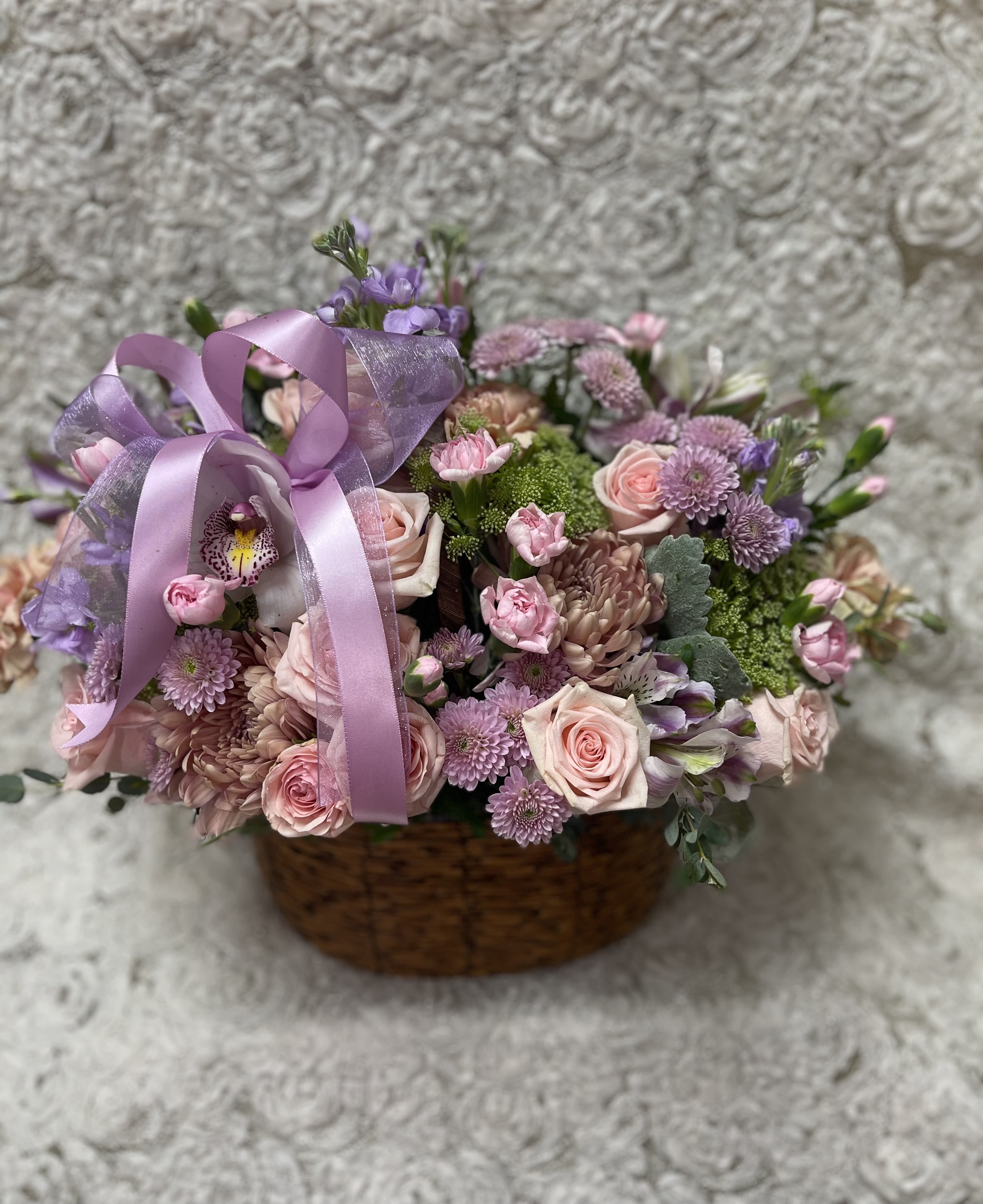 Basket arrangement of pink and lavender flowers with a purple ribbon