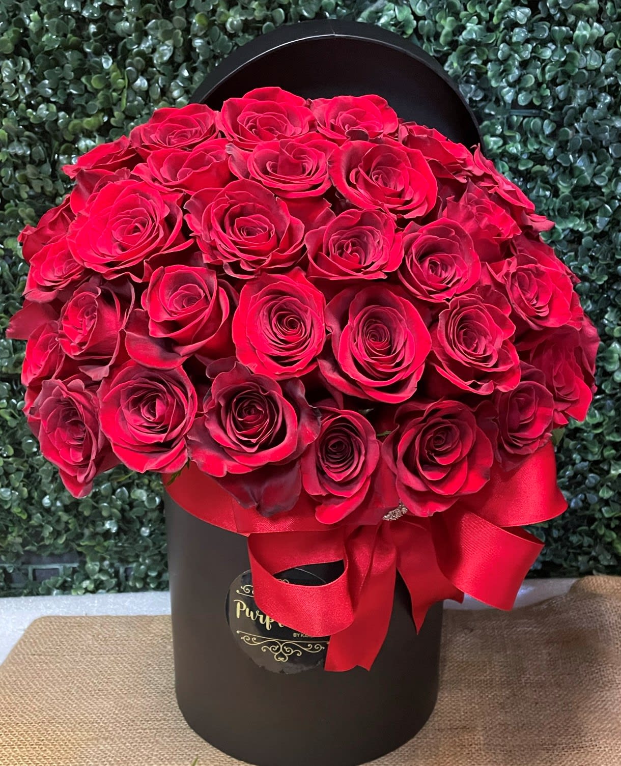 Red roses arranged in a black hat box with a red ribbon