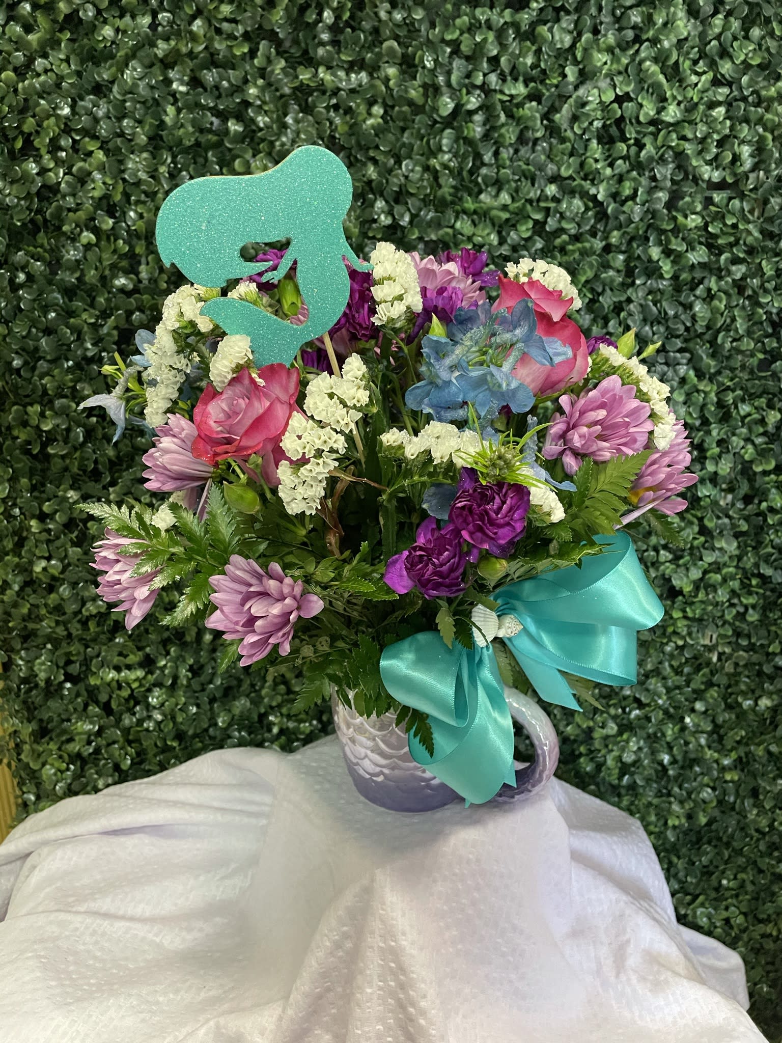 Mixed pink and purple bouquet in a white mug with a teal ribbon