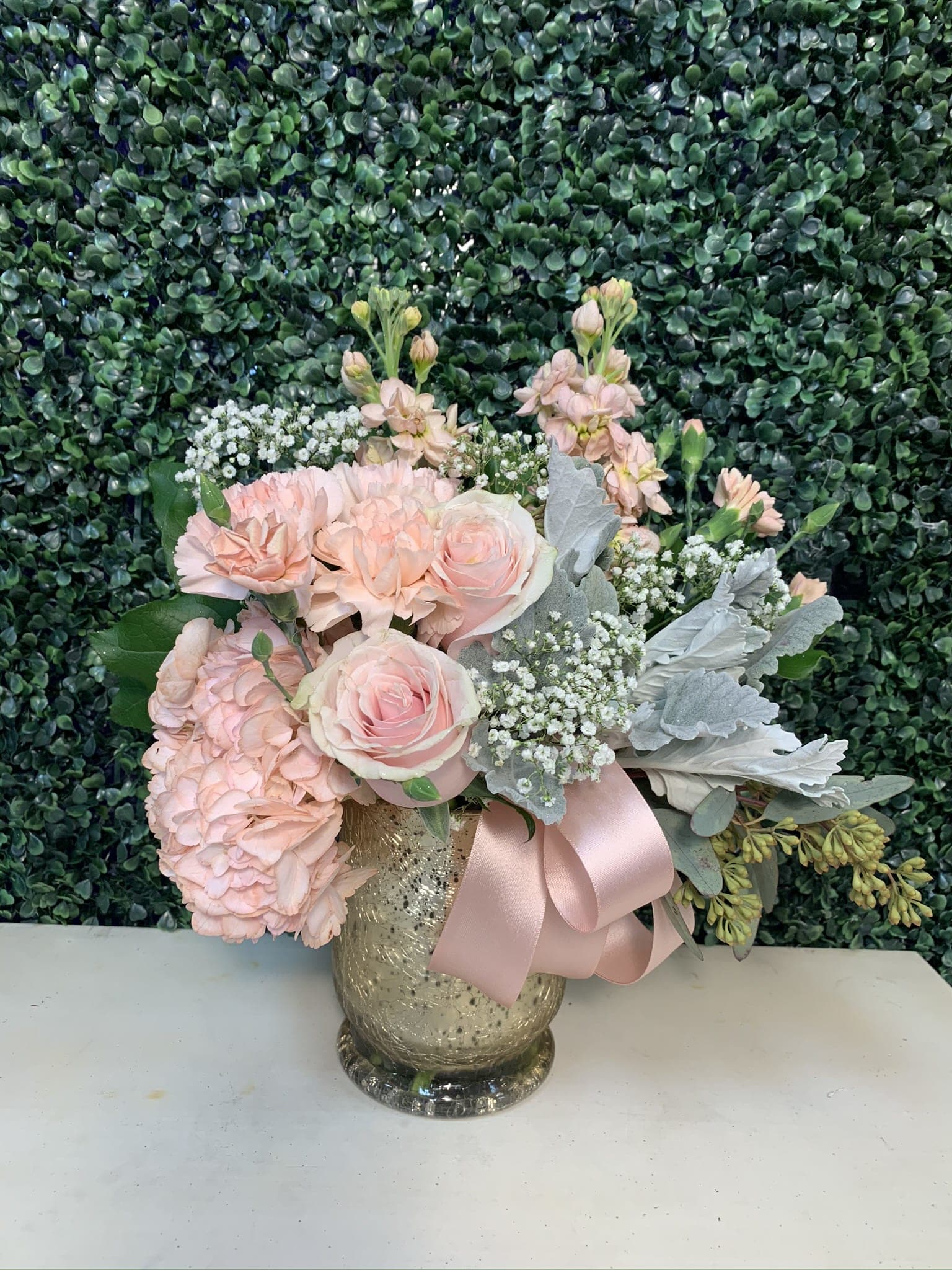 Pink roses and hydrangeas in a gold vase with a pink ribbon