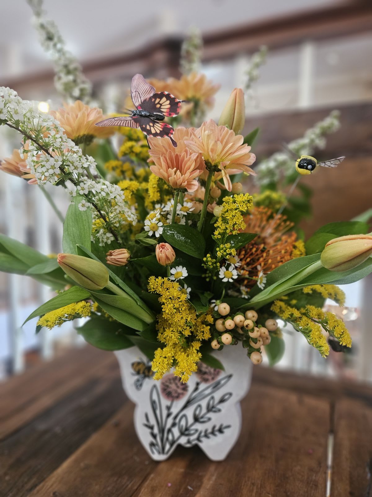 Butterflies and Bees Please Bouquet - This whimsical ceramic butterfly container is filled with daisys, tulips, protea, hypericum berries, solidago and more with butterflies and bees flying about!