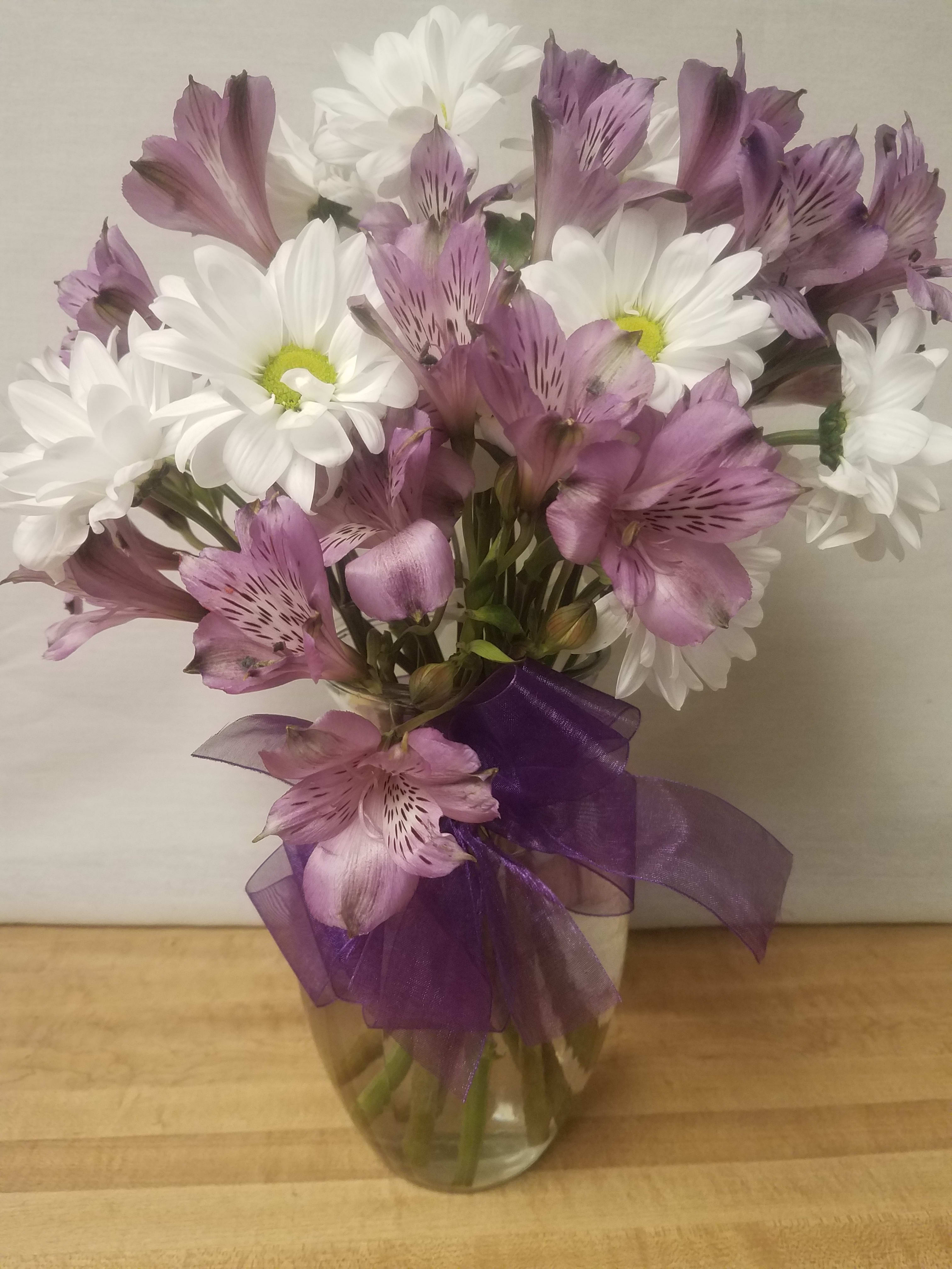 White daisies and purple alstroemeria in a glass vase with a purple ribbon