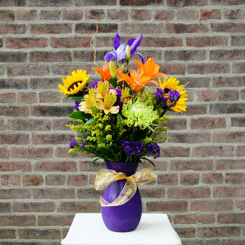 Colorful bouquet in a purple vase with a ribbon bow