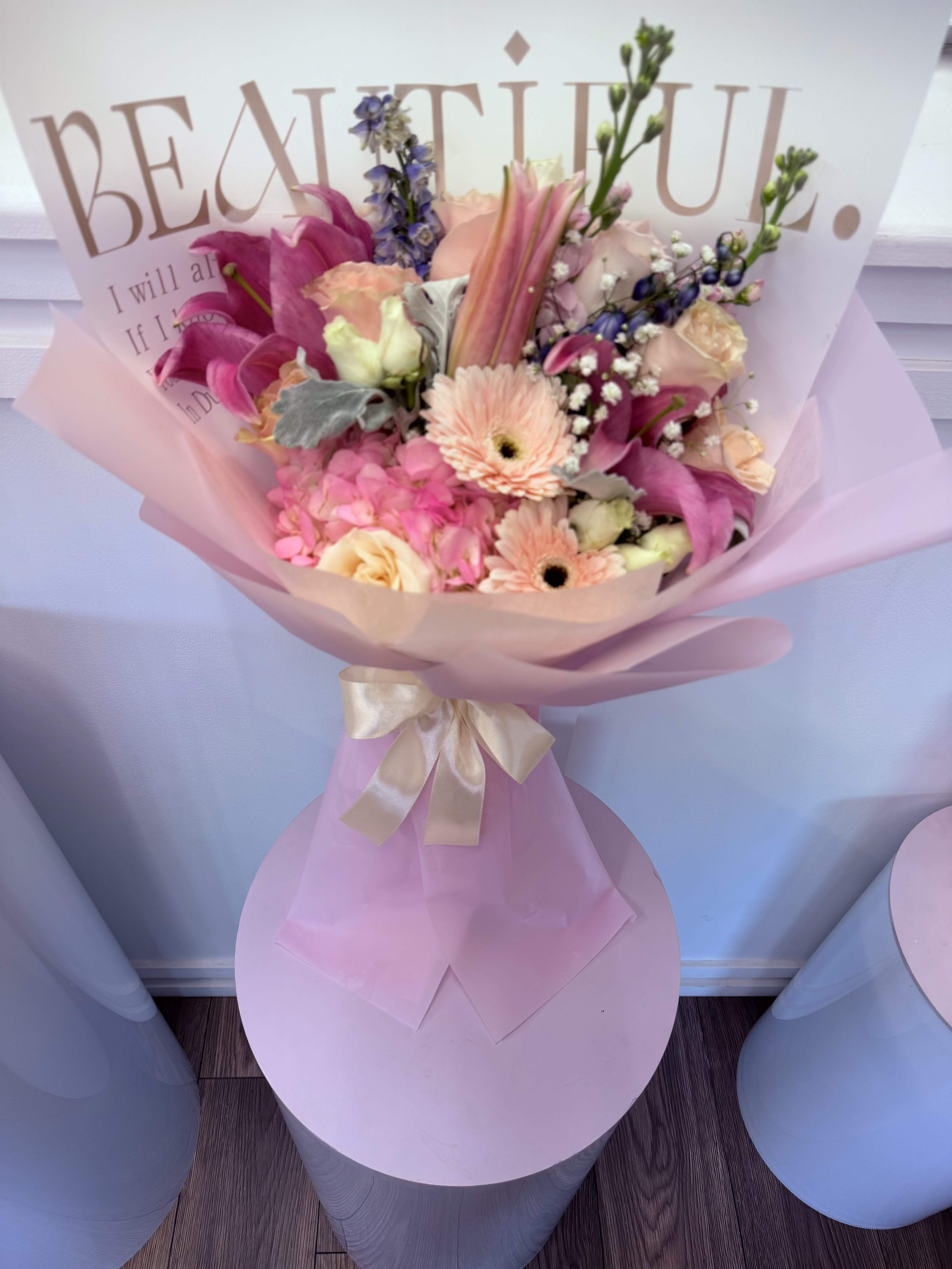 Blush Garden Fantasy - Our Blush Garden Fantasy bouquet is a breathtaking mix of elegance, color, and romance designed to impress at first sight.  This luxurious arrangement features stunning pink lilies, fresh hydrangeas, premium roses in soft tones, seasonal flowers, and lush greenery, all beautifully wrapped in elegant Korean-style paper and finished with a satin ribbon.  Every detail of this bouquet reflects beauty, softness, and sophistication, making it the perfect gift for birthdays, Mother’s Day, celebrations, or simply to brighten someone’s day. 