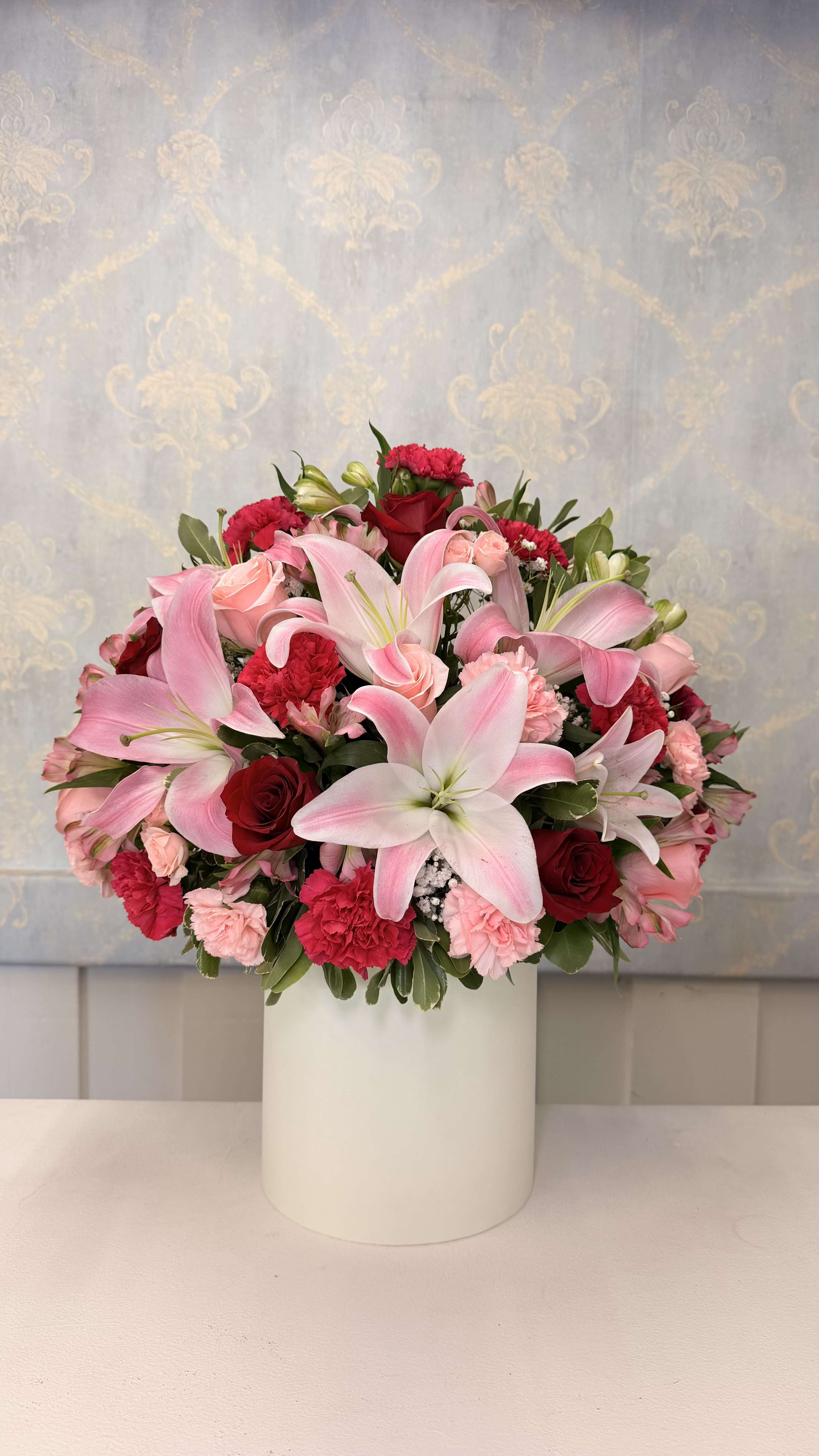 Elegancia Rosada – Arreglo Floral Premium en Base - An elegant and sophisticated floral arrangement, perfect for any special occasion   This design features a beautiful mix of roses, lilies, carnations, alstroemeria, and fresh greenery, using carefully selected seasonal flowers.  Arranged in a vase/base, it is ready to enjoy with no need for an additional container.   Perfect for birthdays, celebrations, or simply to make someone feel special.