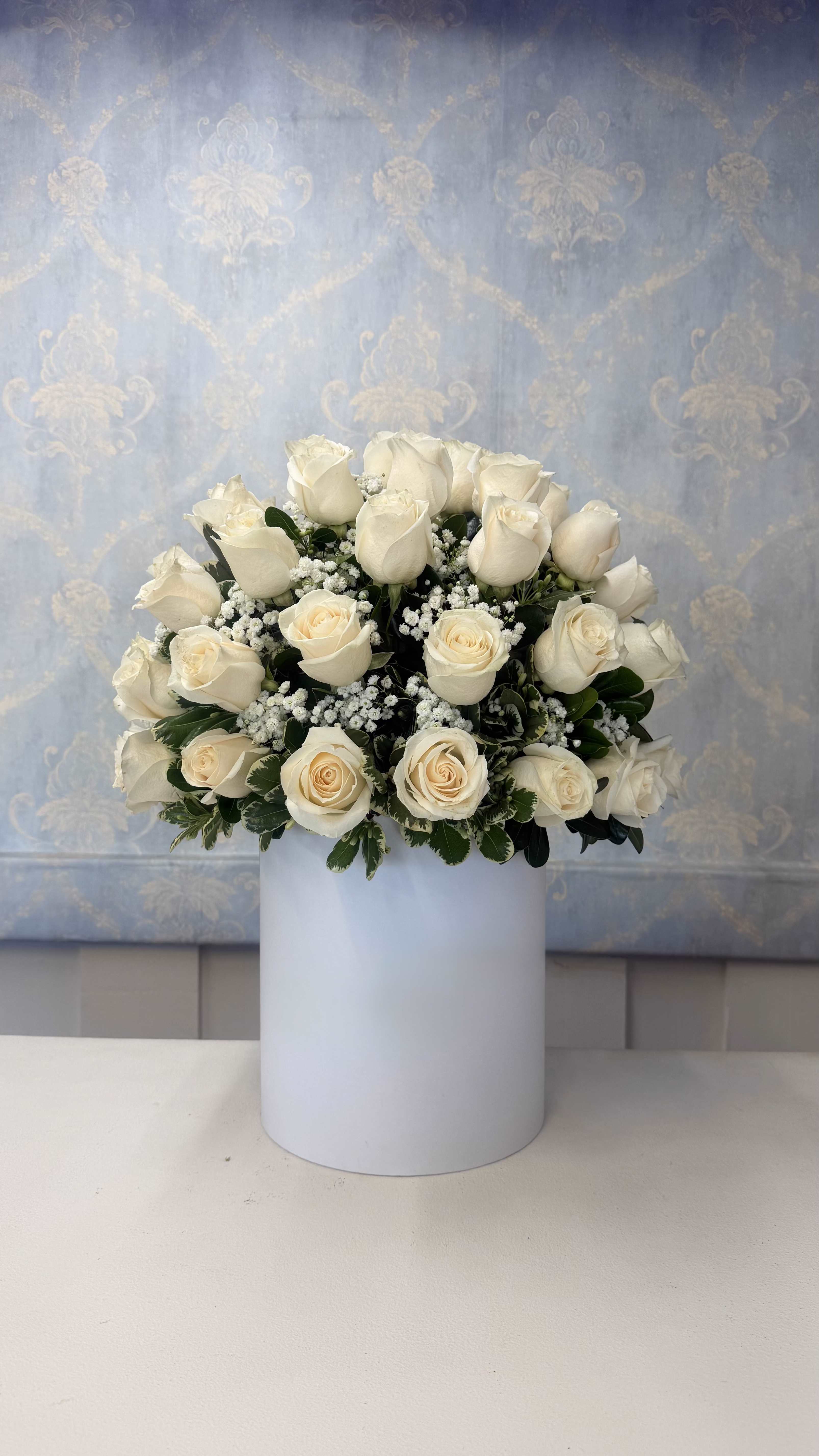 White Elegance – Premium Rose Arrangement - A clean, elegant, and sophisticated floral arrangement designed to express peace, love, and beauty   This beautiful design features fresh white roses, baby’s breath, and green foliage, carefully arranged in a modern elegant vase for a timeless and luxurious presentation.   Perfect for anniversaries, elegant sympathy gestures, birthdays, or any special occasion where you want to impress with a refined and timeless gift.