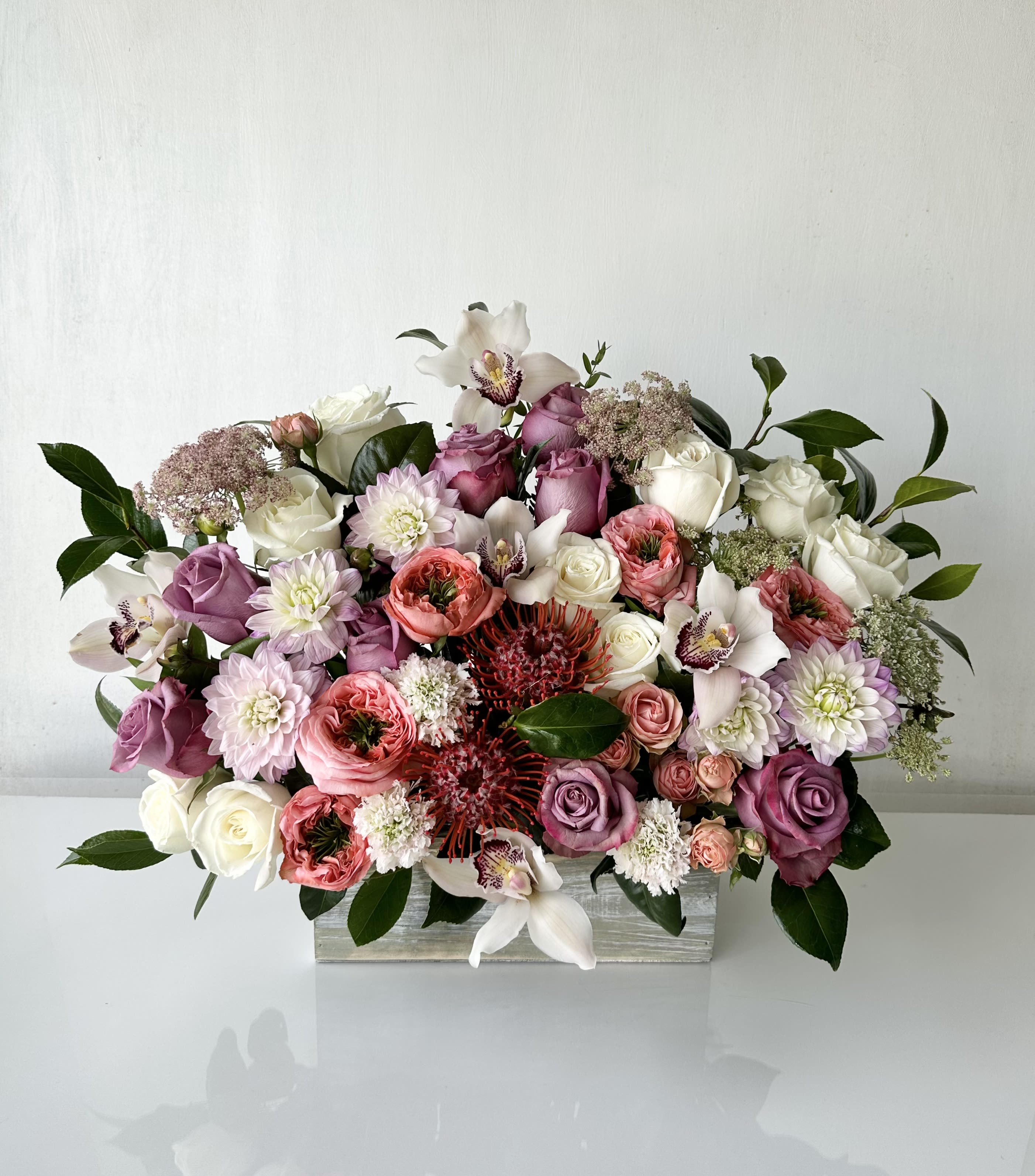 Box of Joy - A wooden box of colorful fresh cut flowers, including a variety of roses, dahlia, spray roses, pin cushions, scabiosa, cymbidium orchids, queen ann's lace, and camelia leaves. This arrangement brings positivity to occasions including Congratulating, Thanking, Mother's Day, and Birthdays. Availability: 24 hours notice  Dimensions: Approximately 21" H x 25" W        