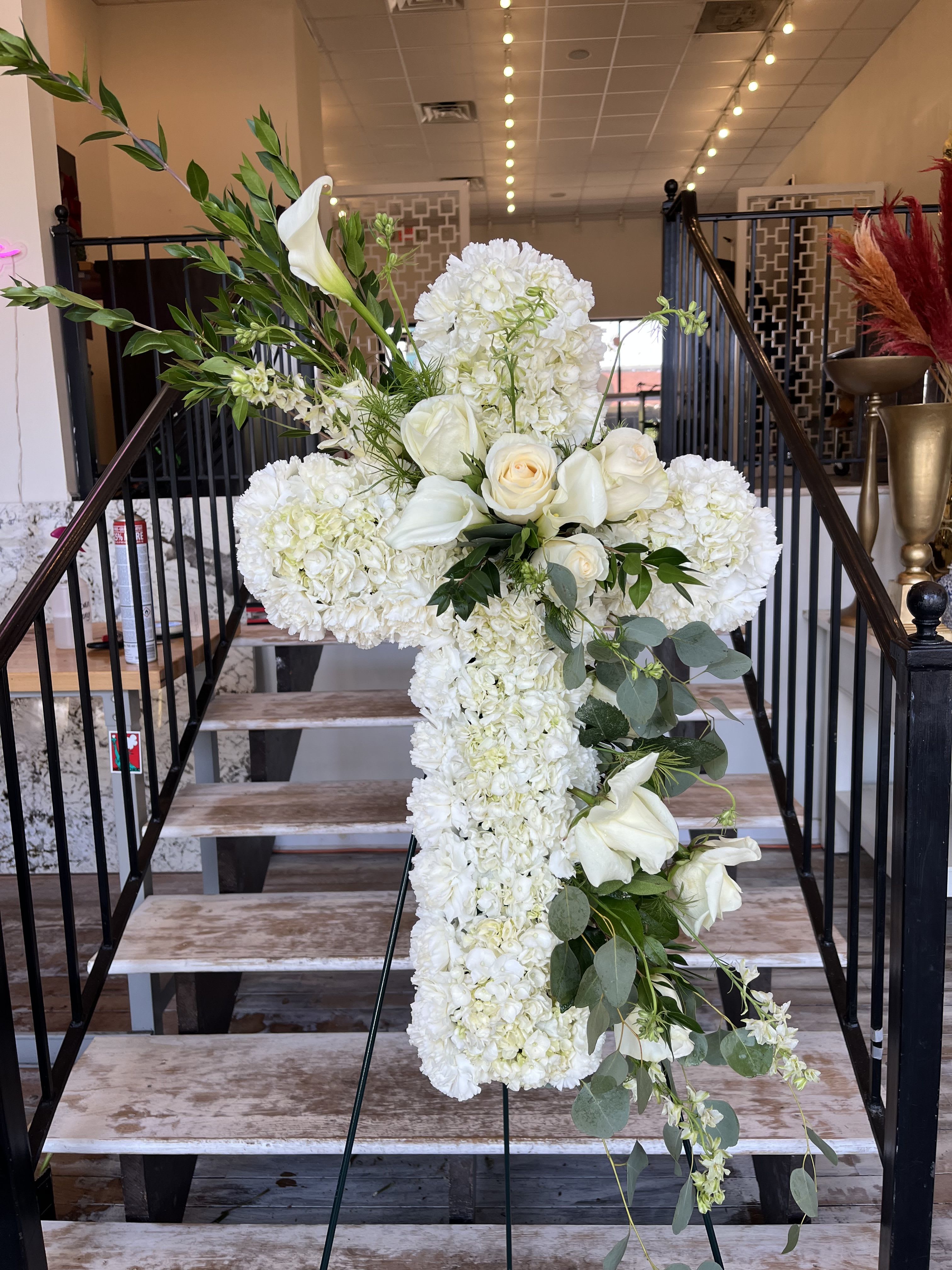 White floral cross arrangement on an easel with roses and calla lilies