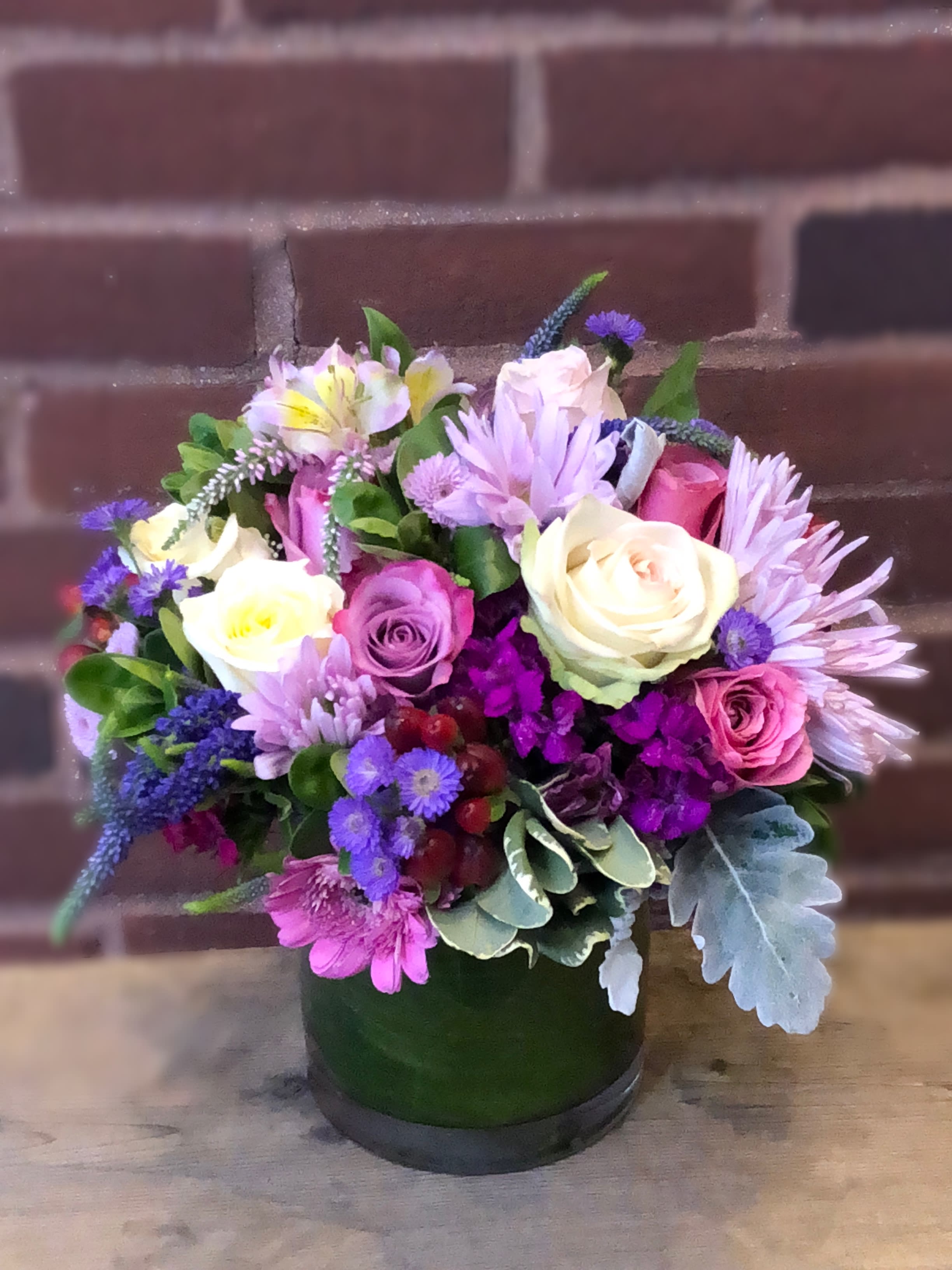 Mixed bouquet of roses and purple flowers in a green vase