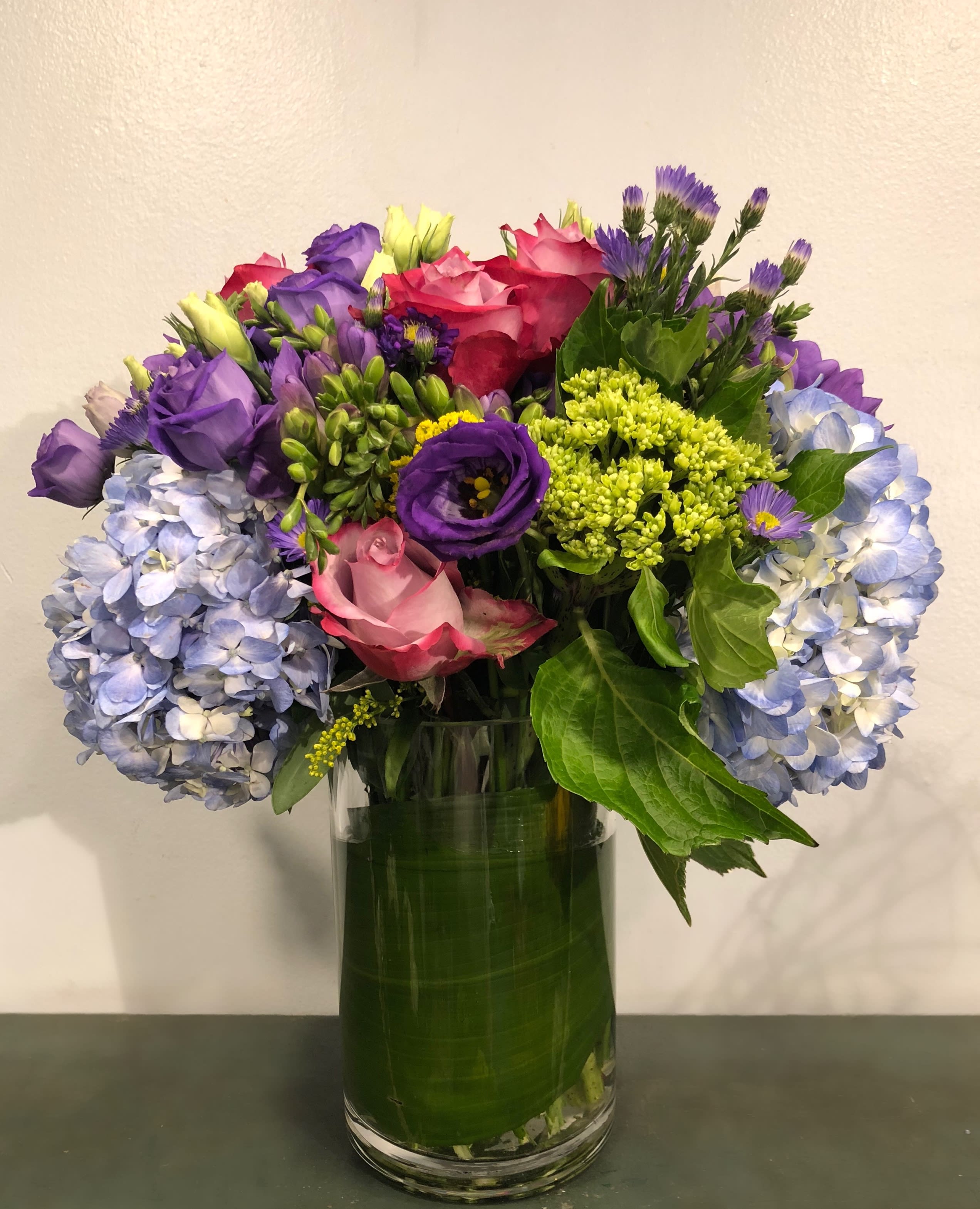 Mixed bouquet of roses, hydrangeas, and purple flowers in a glass vase